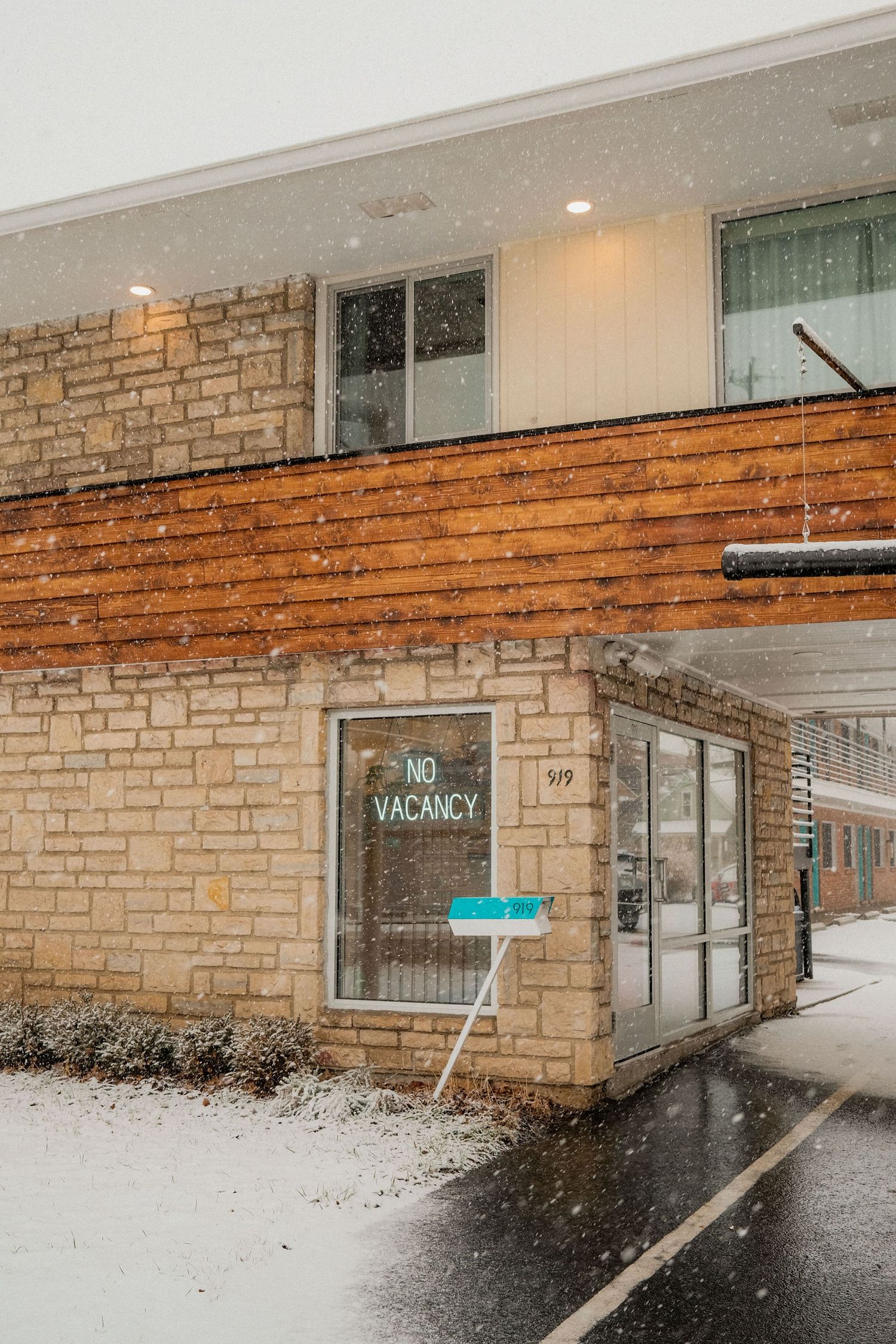 Snow falls outside a brick motel building with a vintage vacancy sign in winter.