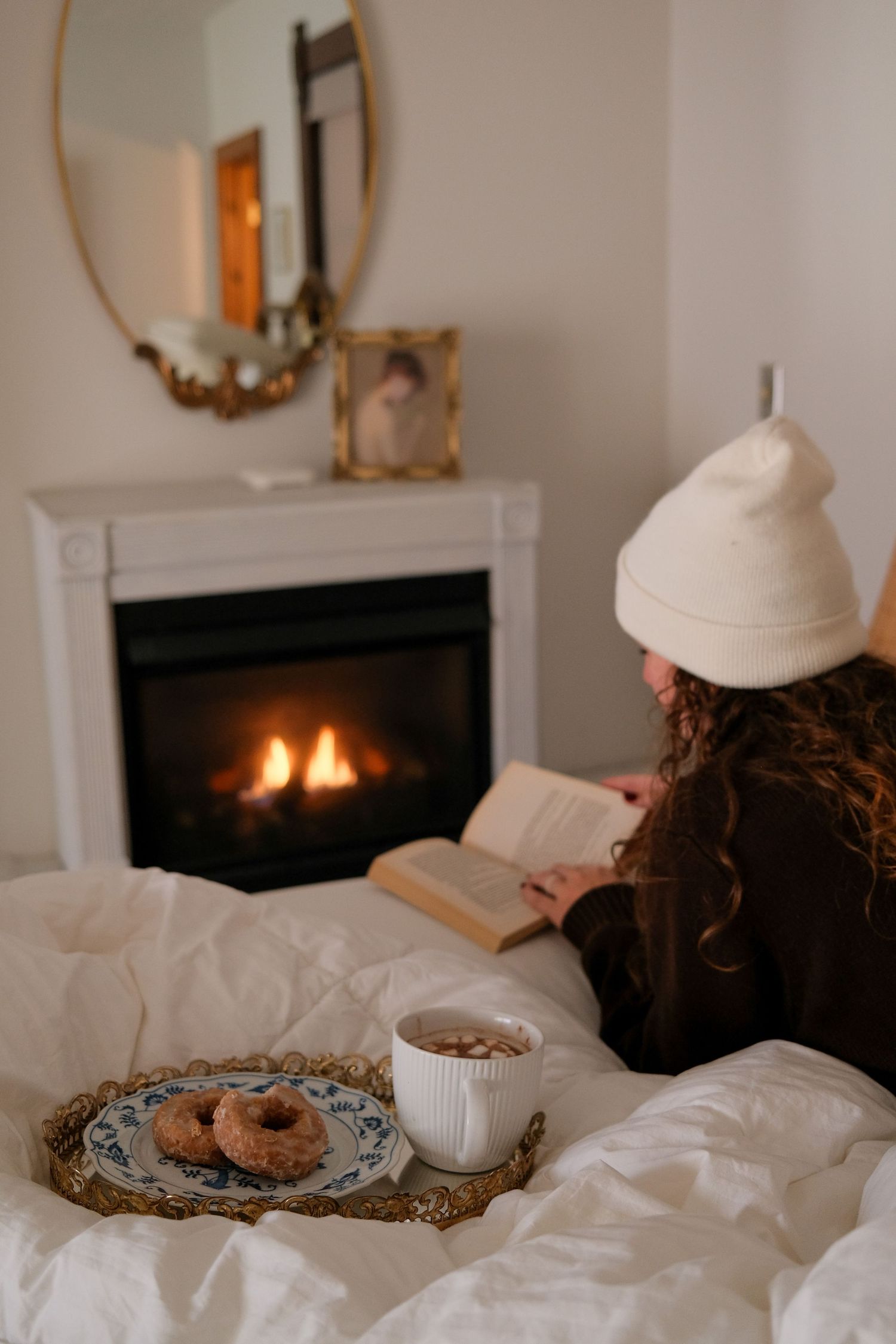 Breakfast in bed setup with pastries and tea next to a warm fireplace.