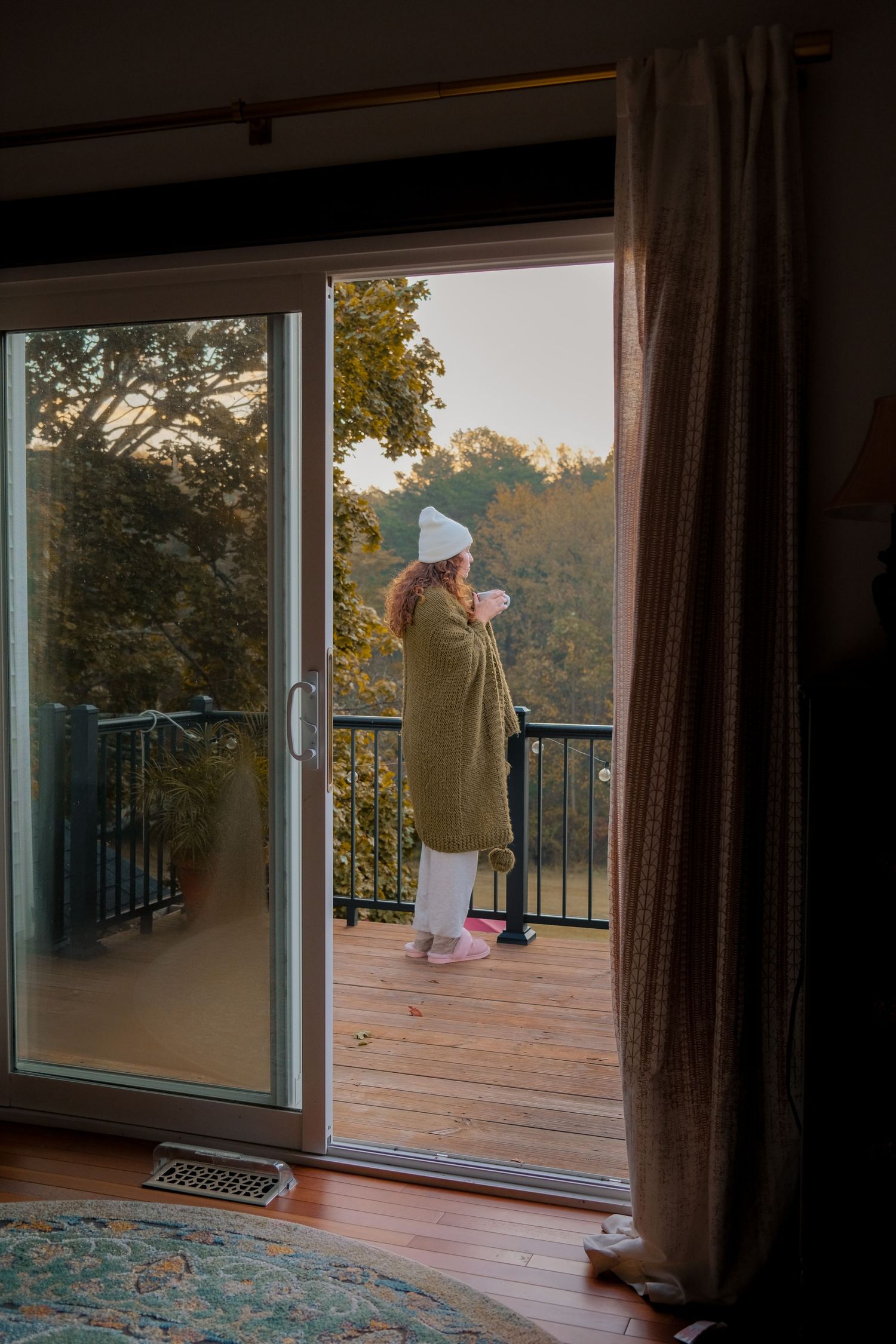 Sliding glass doors open to a wooden deck with outdoor furniture at dusk.