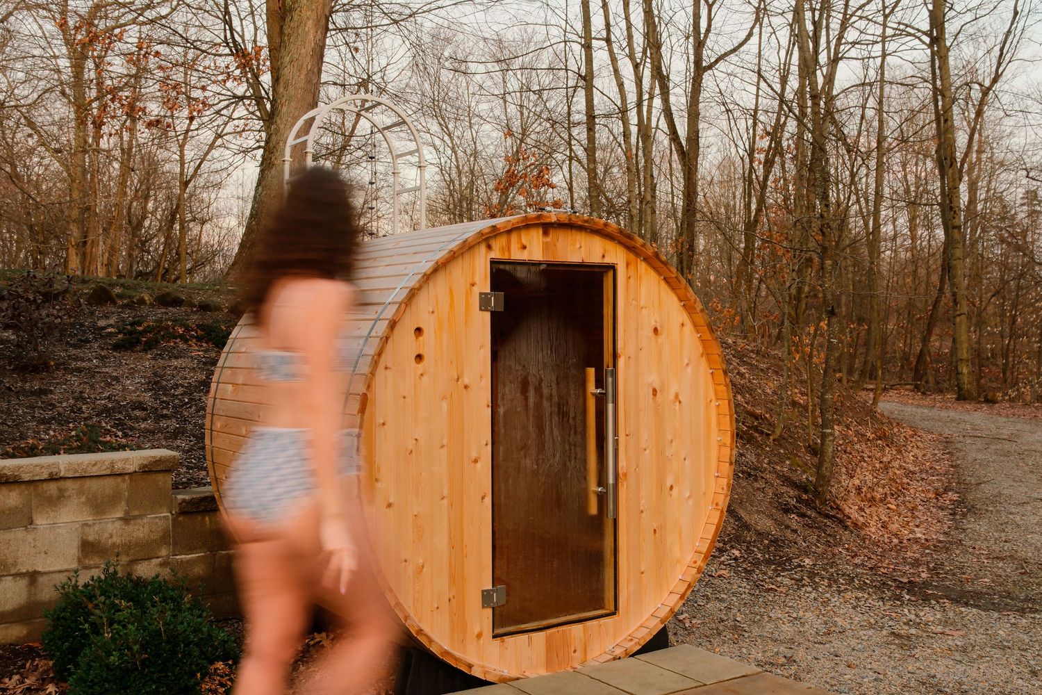 A wooden barrel sauna nestled in a wooded area during autumn with multiple views of its exterior and interior.