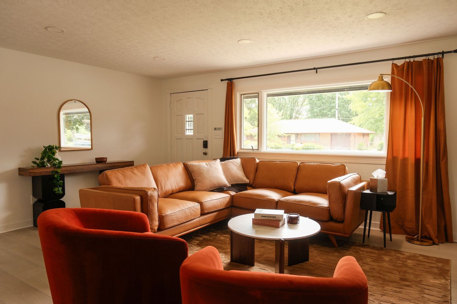 Bright living room with tan leather sectional sofa, orange accent chairs, wood coffee table, and warm curtains.