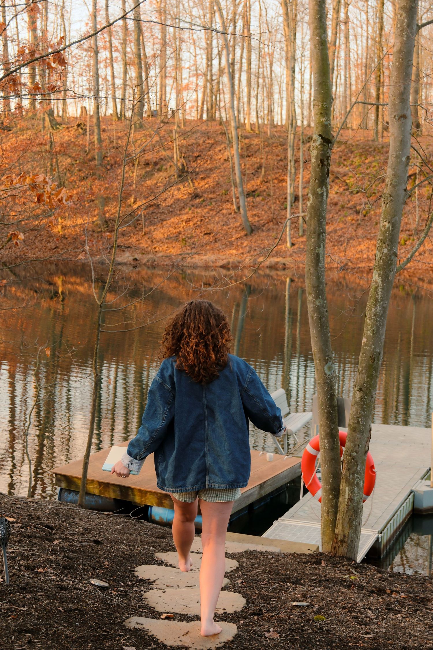Figure walking along a lakeside path through autumn trees at sunset.