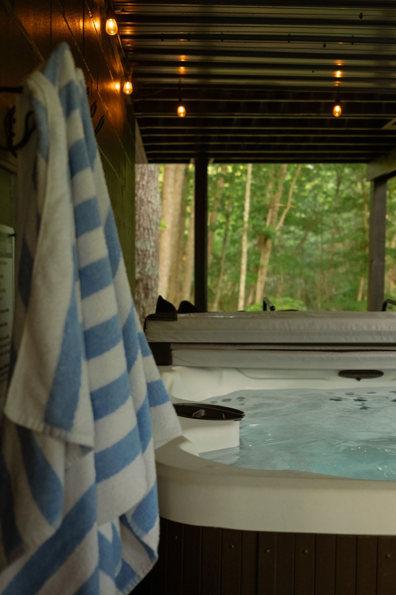 Hot tub with blue and white striped towels on covered deck at dusk.