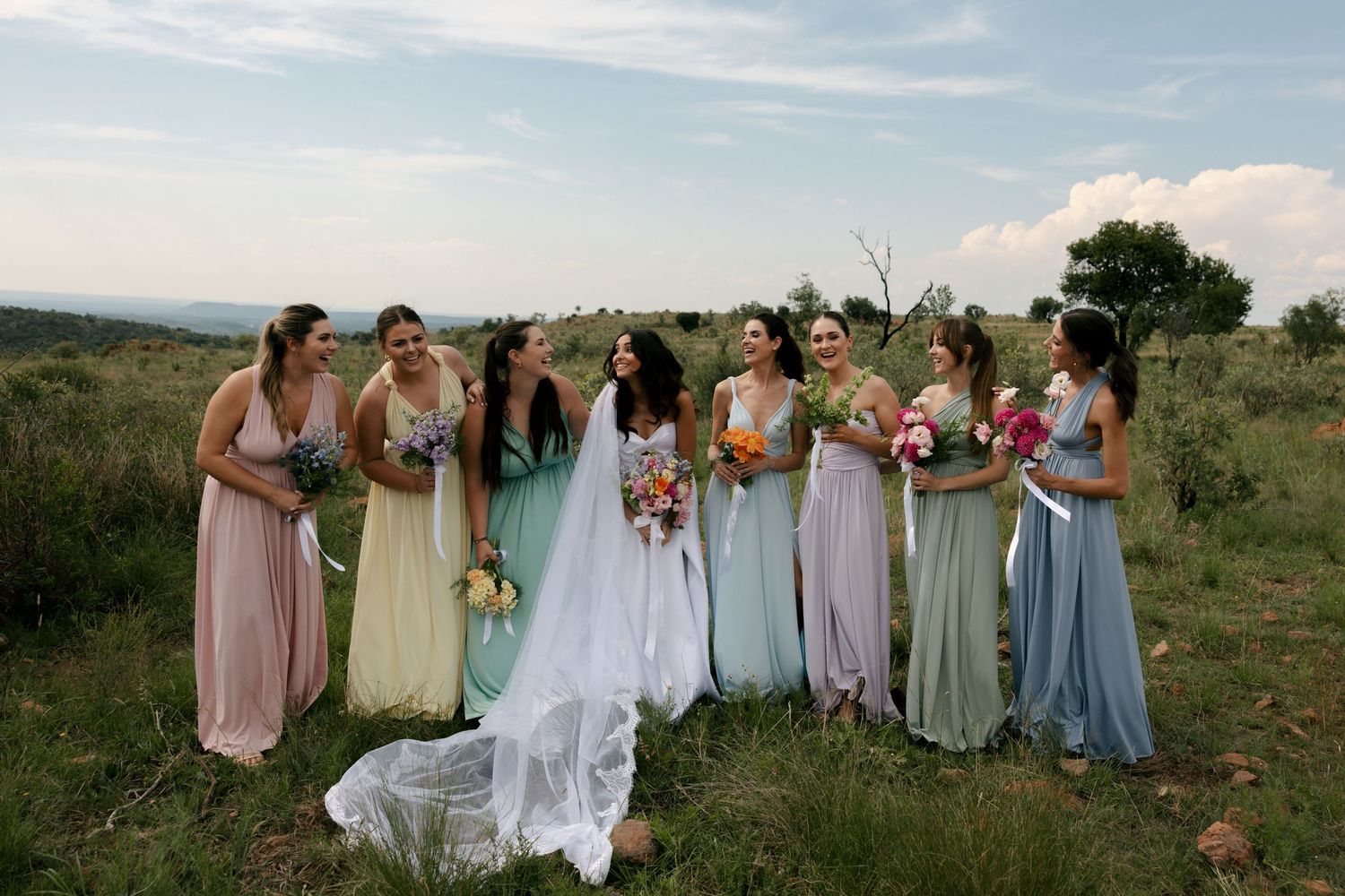 bride and her bridemaids standing on a hill top having a laugh