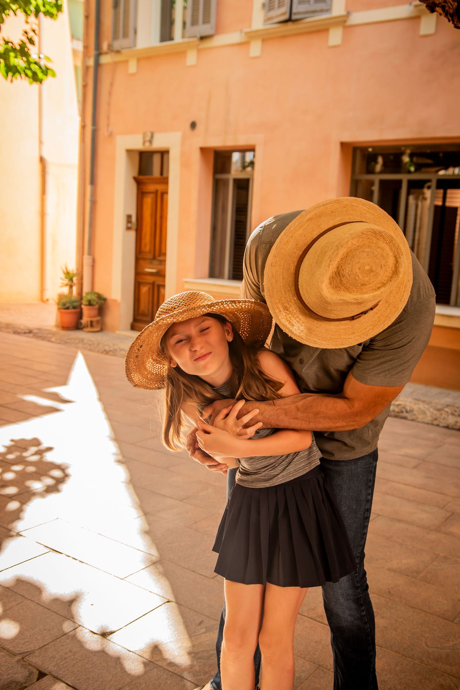 Couple sharing a playful romantic moment outdoors in warm sunlight by a peach-colored building.