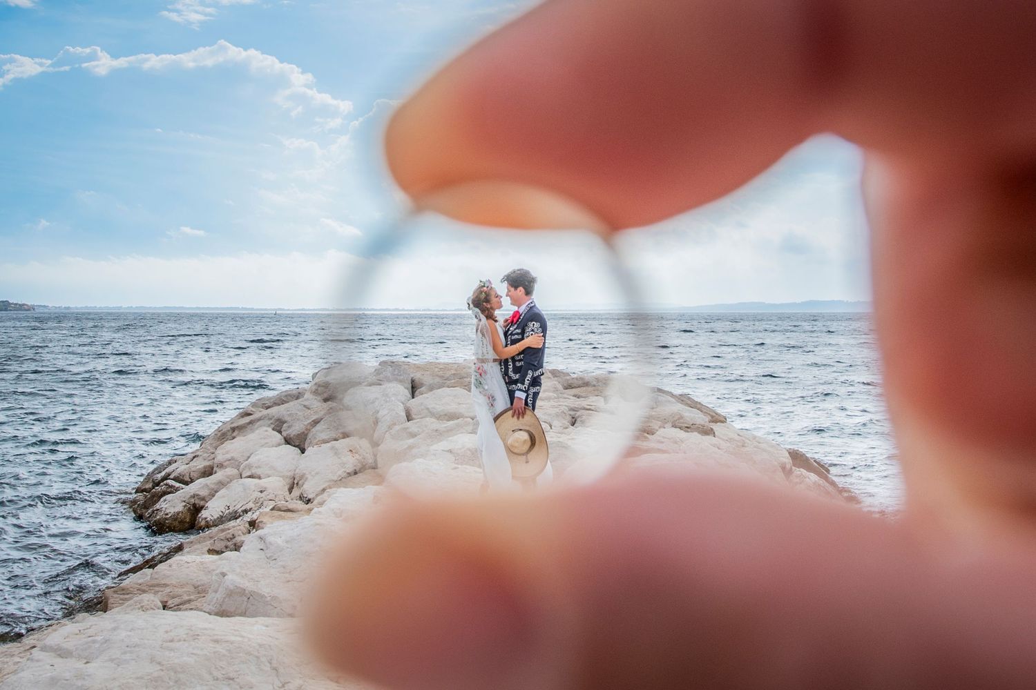 Creative ring photo framing couple embracing on rocky ocean coastline.