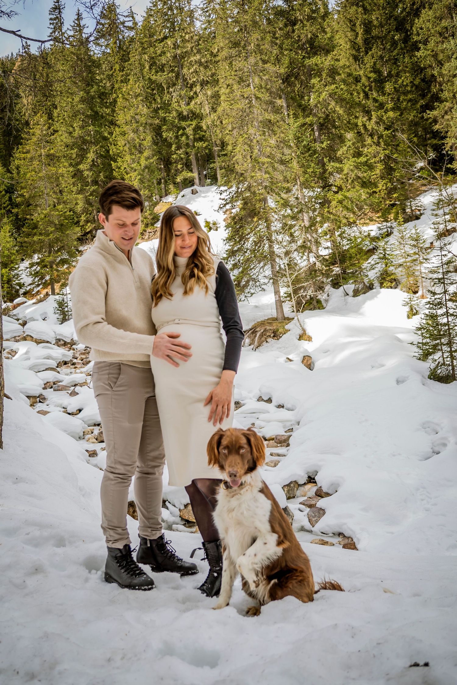 A couple poses with their dog in a snowy winter forest landscape.