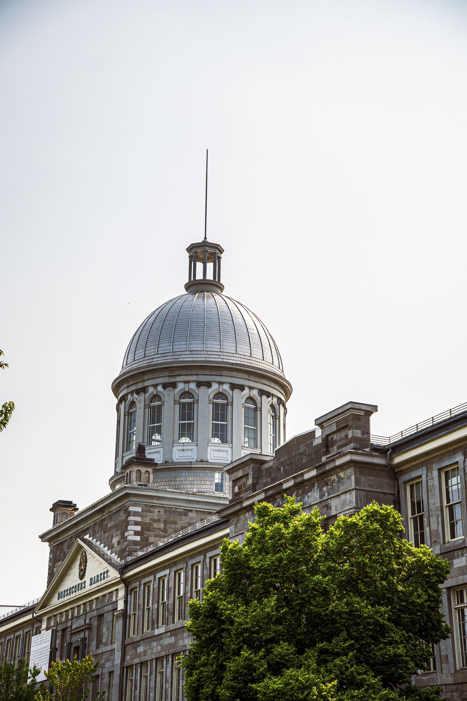 Ornate gray stone building with classical architecture featuring a silver domed cupola and arched windows against pale sky.