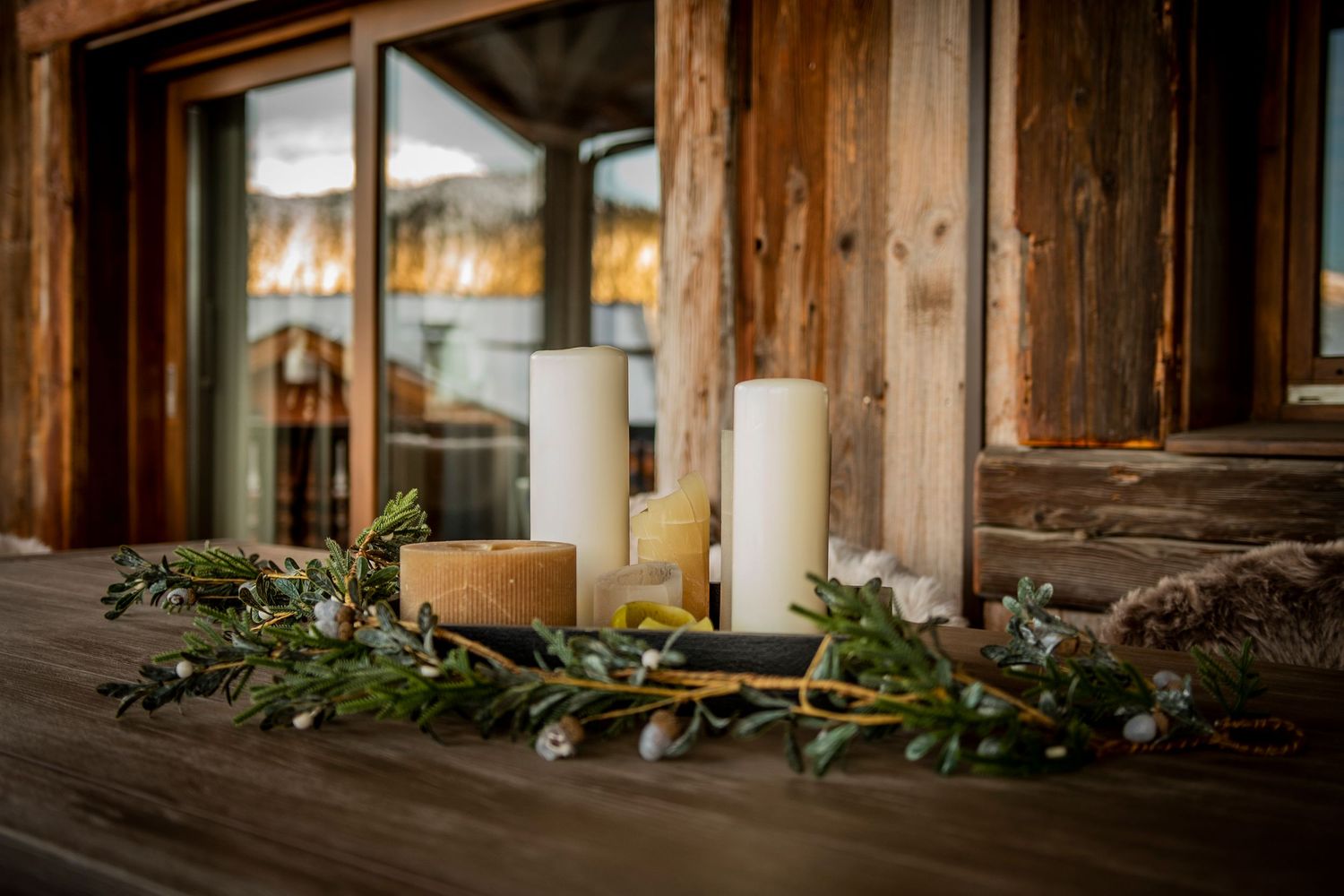 A rustic wooden dining room decorated for a winter wedding with evergreen garlands and white candles on the tables.