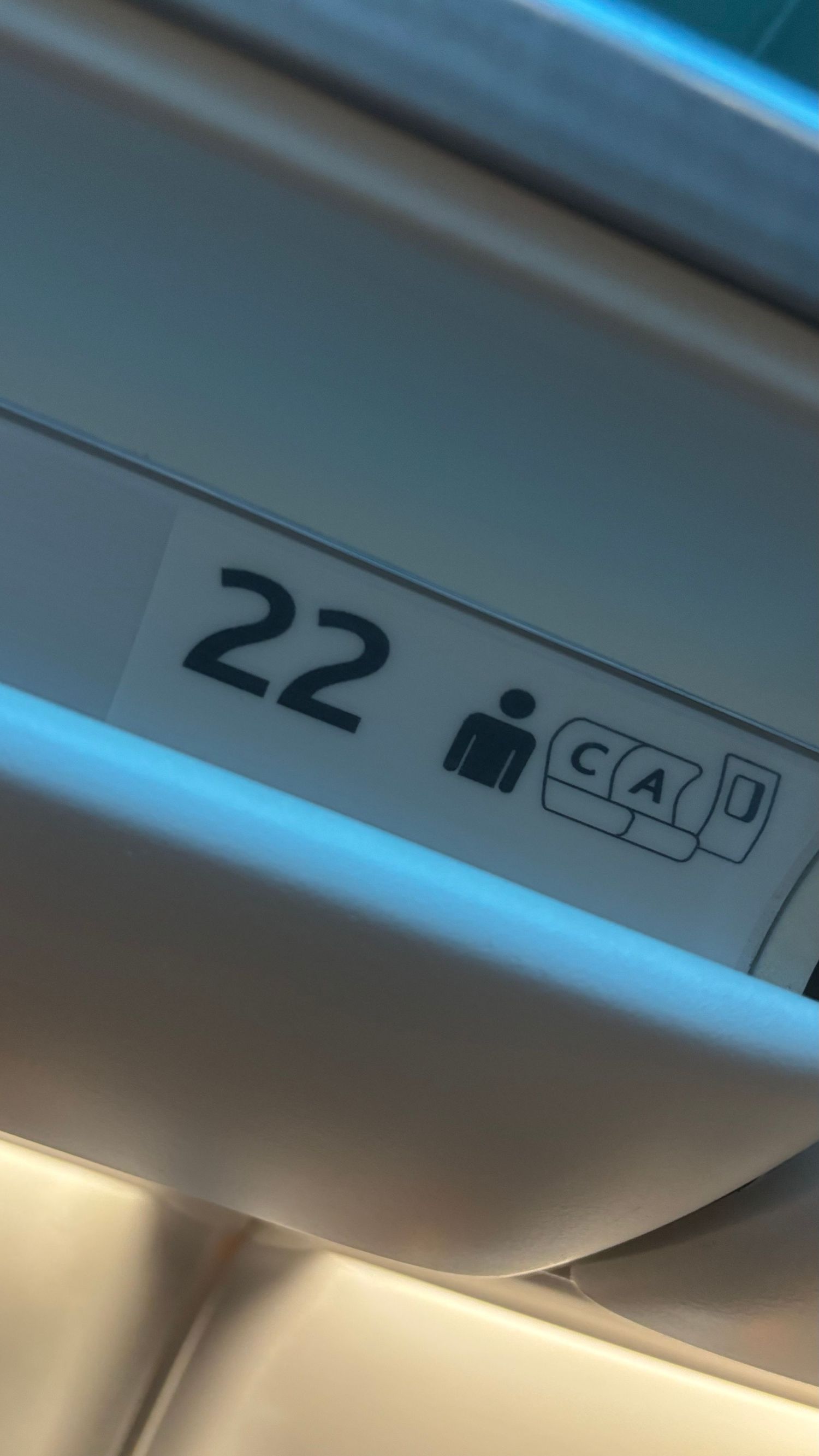 Airplane cabin interior showing overhead compartment signs and panels illuminated by blue ambient lighting.