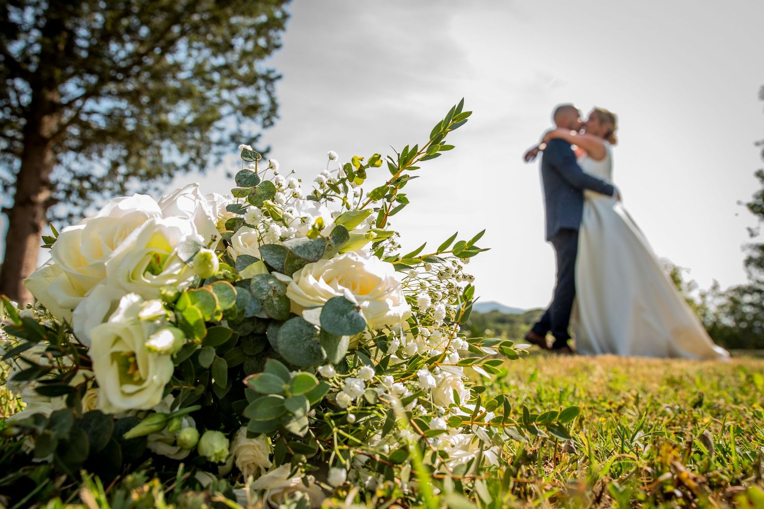 Elegant white floral bouquet with lush greenery against a softly blurred outdoor background.