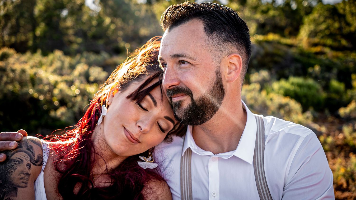 Romantic wedding couple embracing against natural outdoor backdrop at sunset.