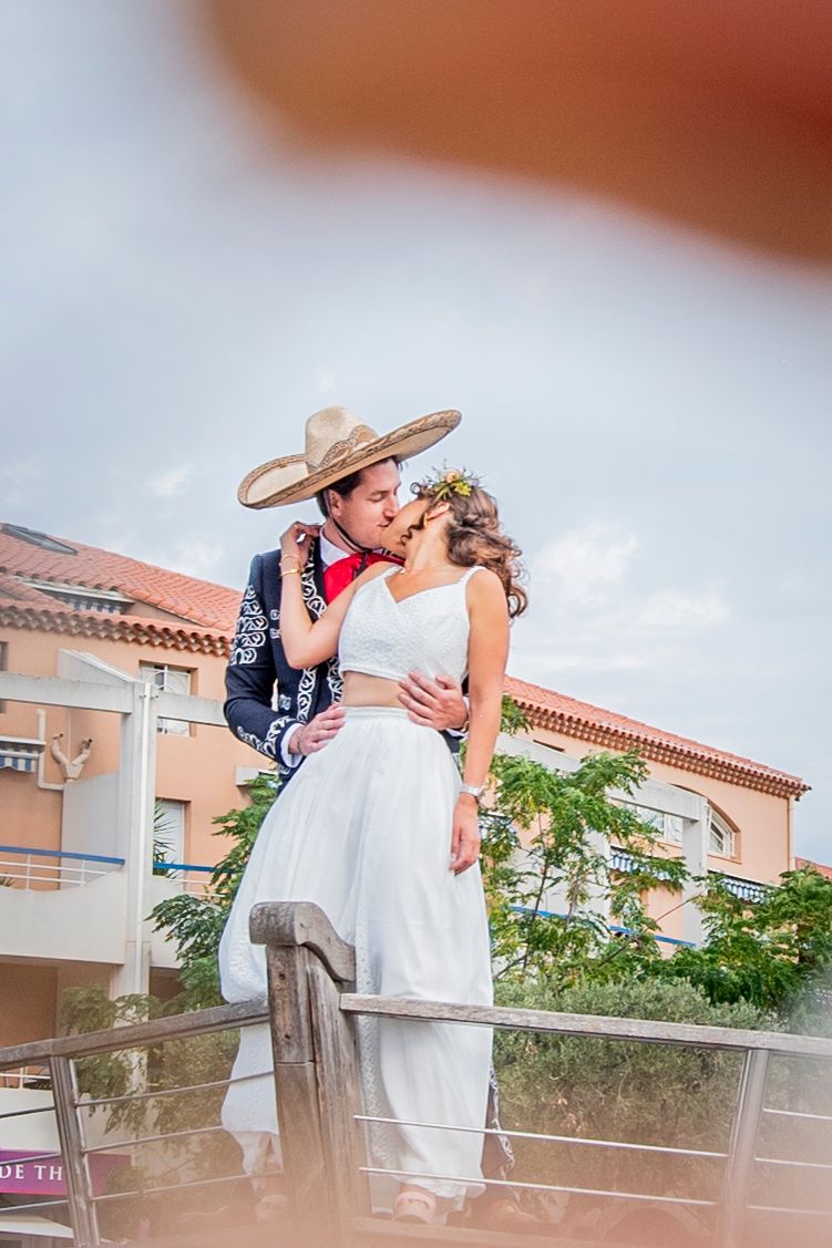 Newlywed couple sharing romantic kiss on balcony with groom wearing traditional Mexican sombrero.