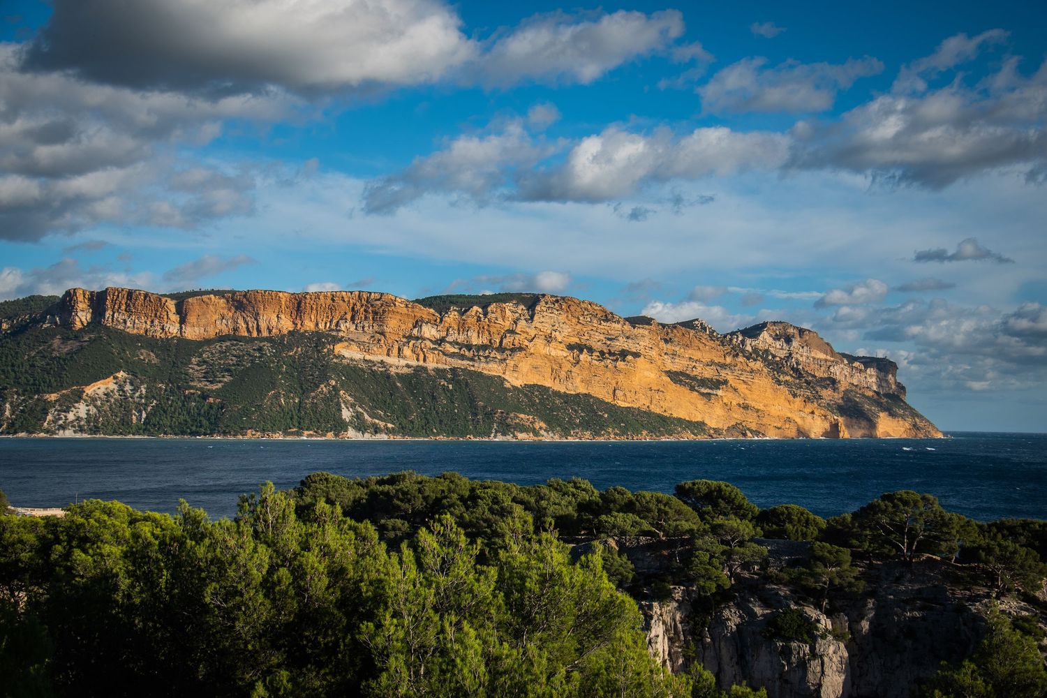 Dramatic cliffs of Calanques National Park rise above the Mediterranean Sea near Marseille under a blue cloudy sky.