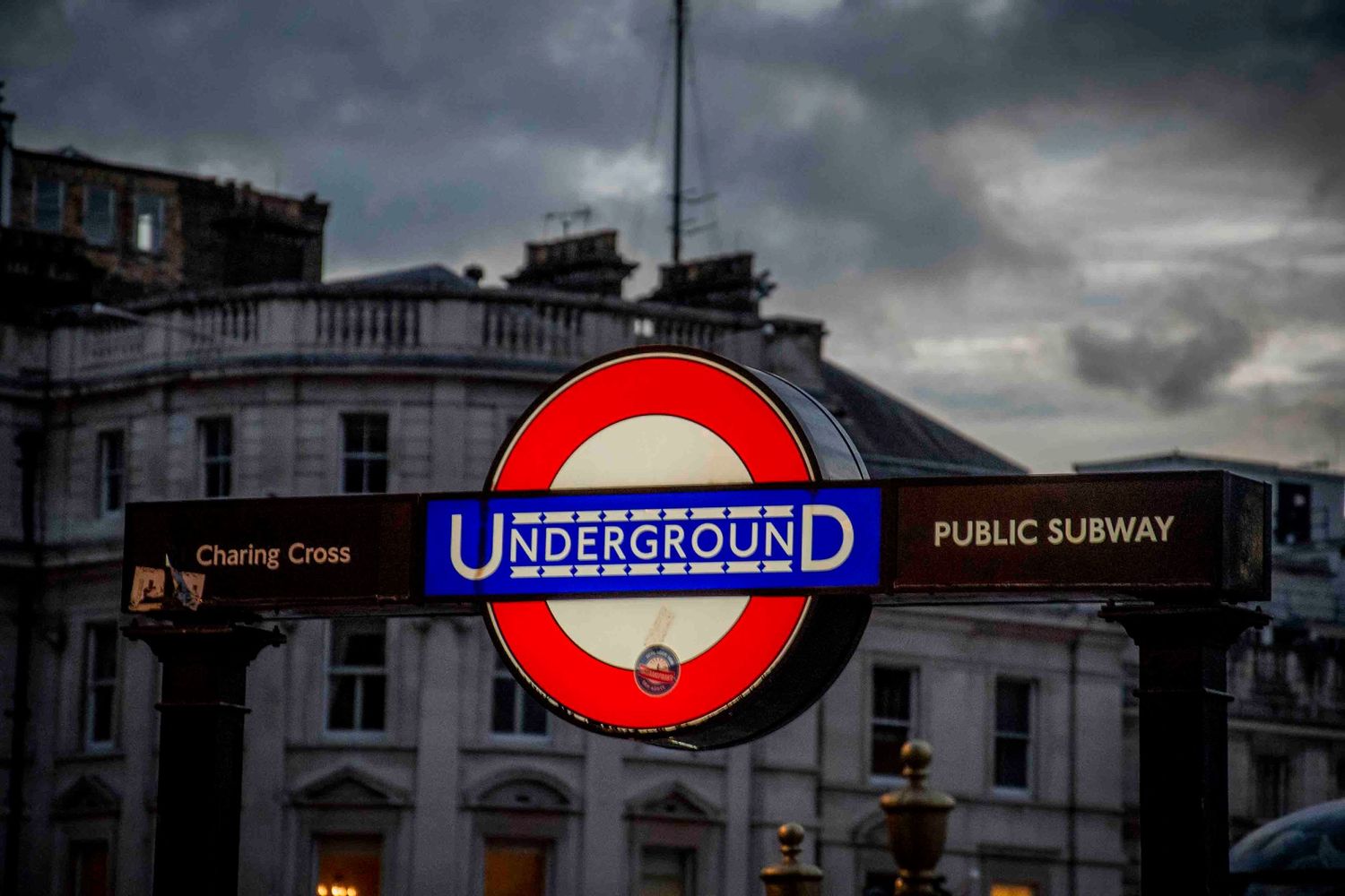 Series of London Underground signs and entrances under moody storm clouds.