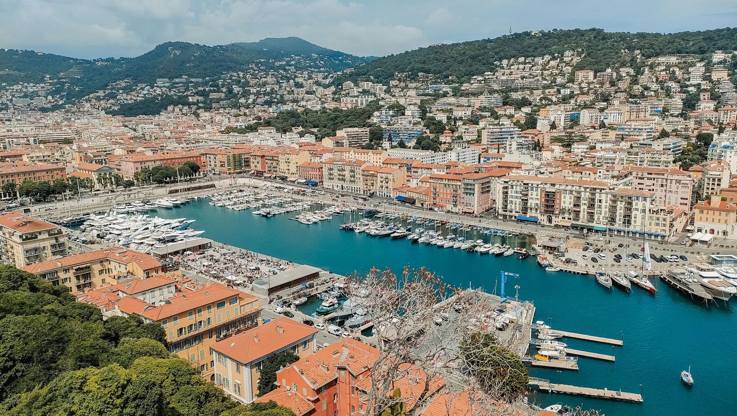 Aerial view of Nice harbor in France with luxury yachts docked along the Mediterranean coastline and terracotta rooftops.