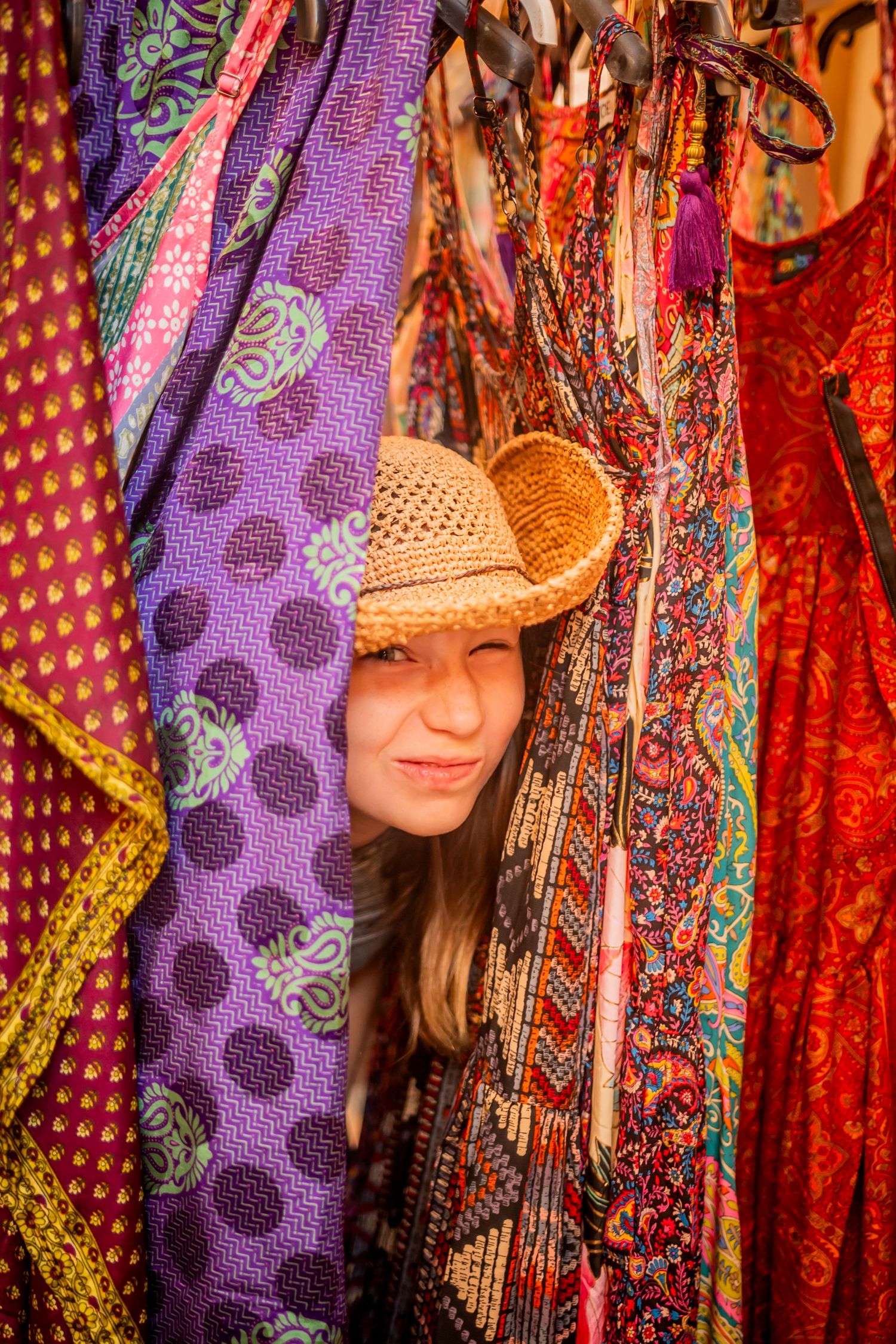 Colorful display of purple patterned fabrics and straw hats at an outdoor market.