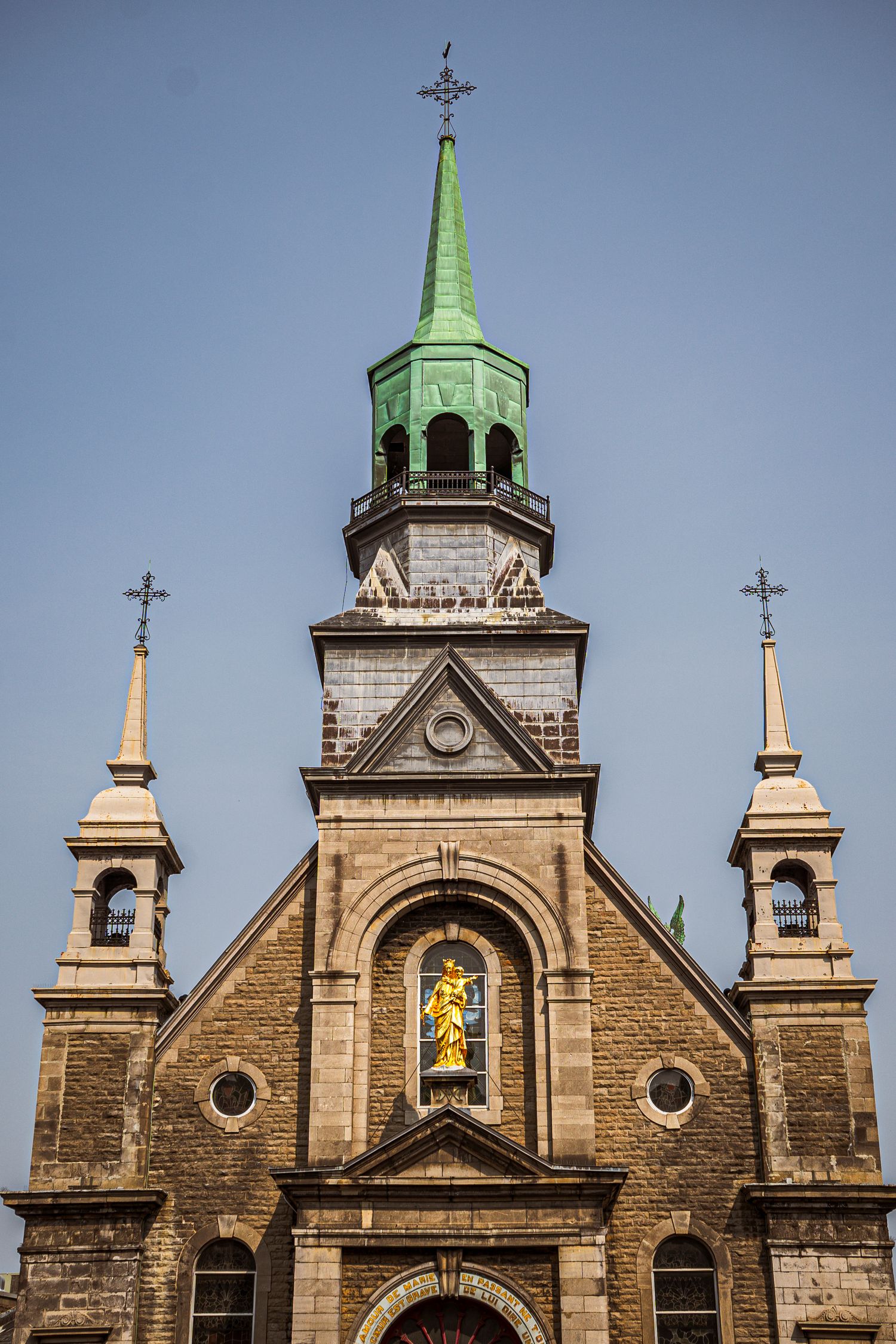 Three gothic church spires with crosses and green copper domes against a blue sky showcase architectural details.