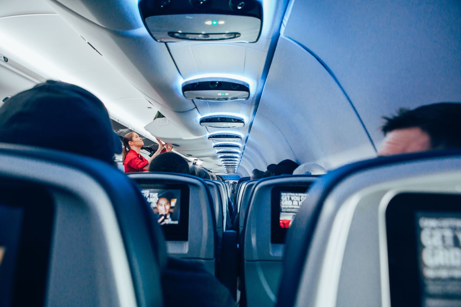 Interior view down airplane aisle showing overhead compartments and passenger seats with blue lighting.