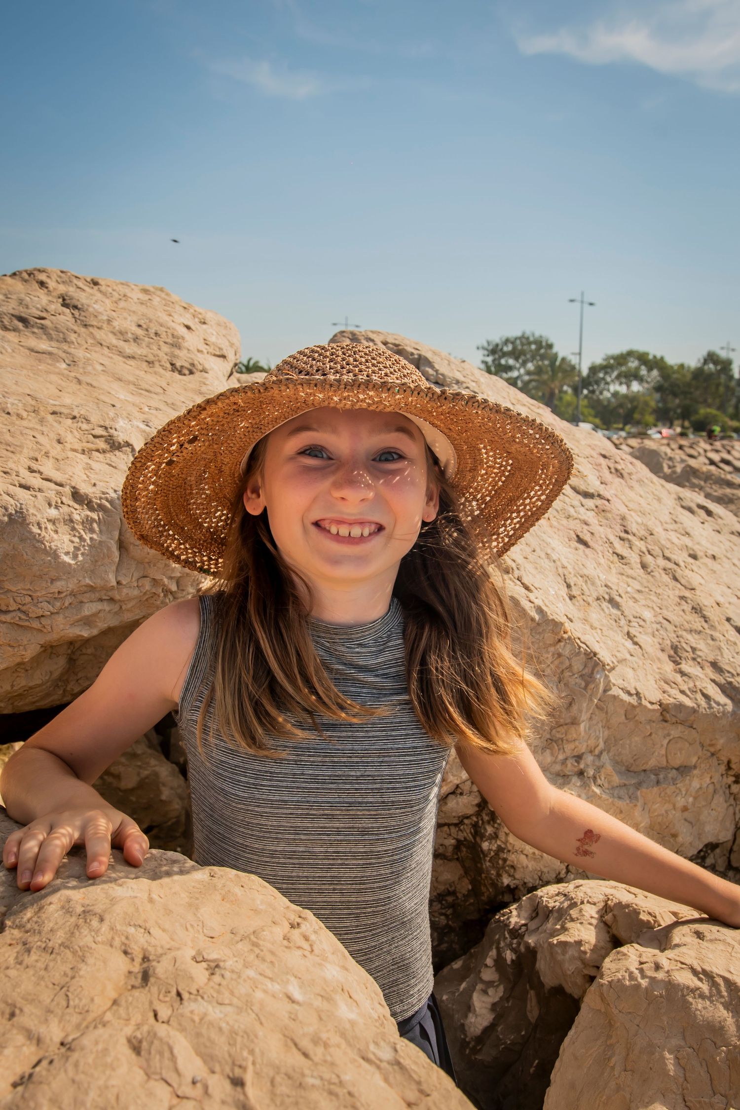 Person wearing straw hat exploring rocky coastal formations on sunny summer day.