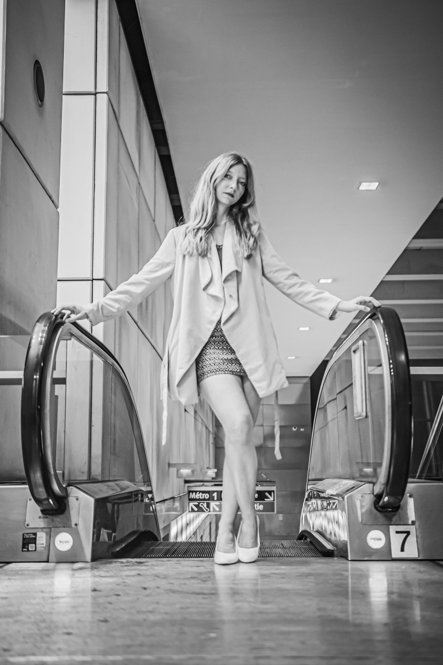 Woman posing playfully at entrance of escalator in urban setting.