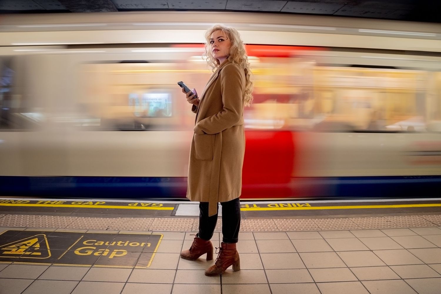 Person stands on subway platform with motion-blurred train in background.