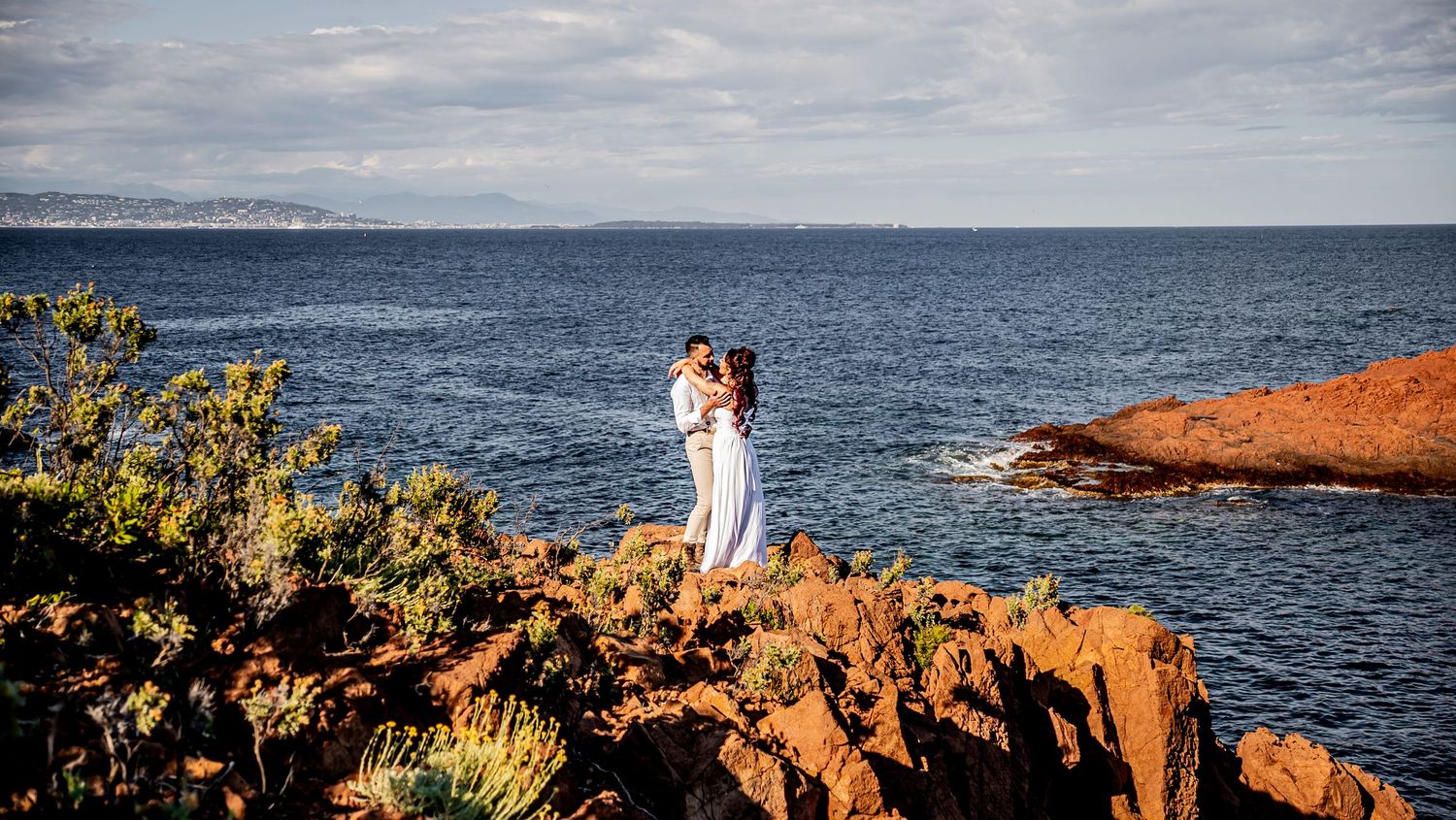 A breathtaking coastal vista shows rocky cliffs meeting the blue ocean under cloudy skies.