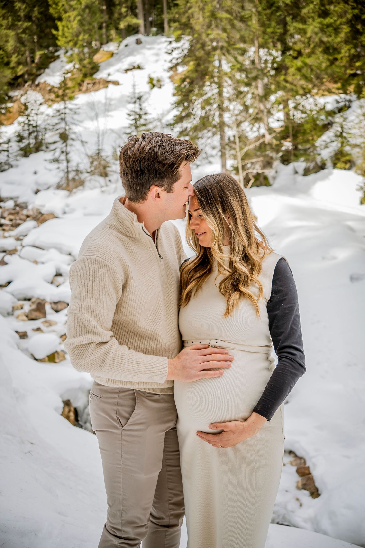 Couple embraces in romantic winter engagement shoot against snowy forest backdrop.