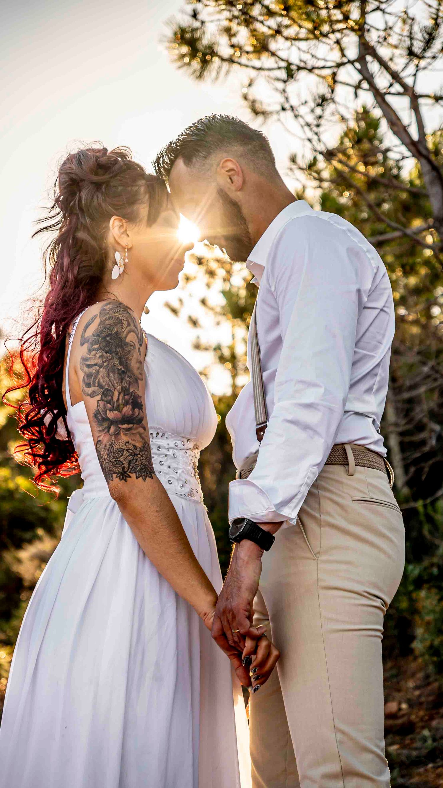 A romantic couple in wedding attire share tender moments at sunset with beautiful golden light filtering through trees.