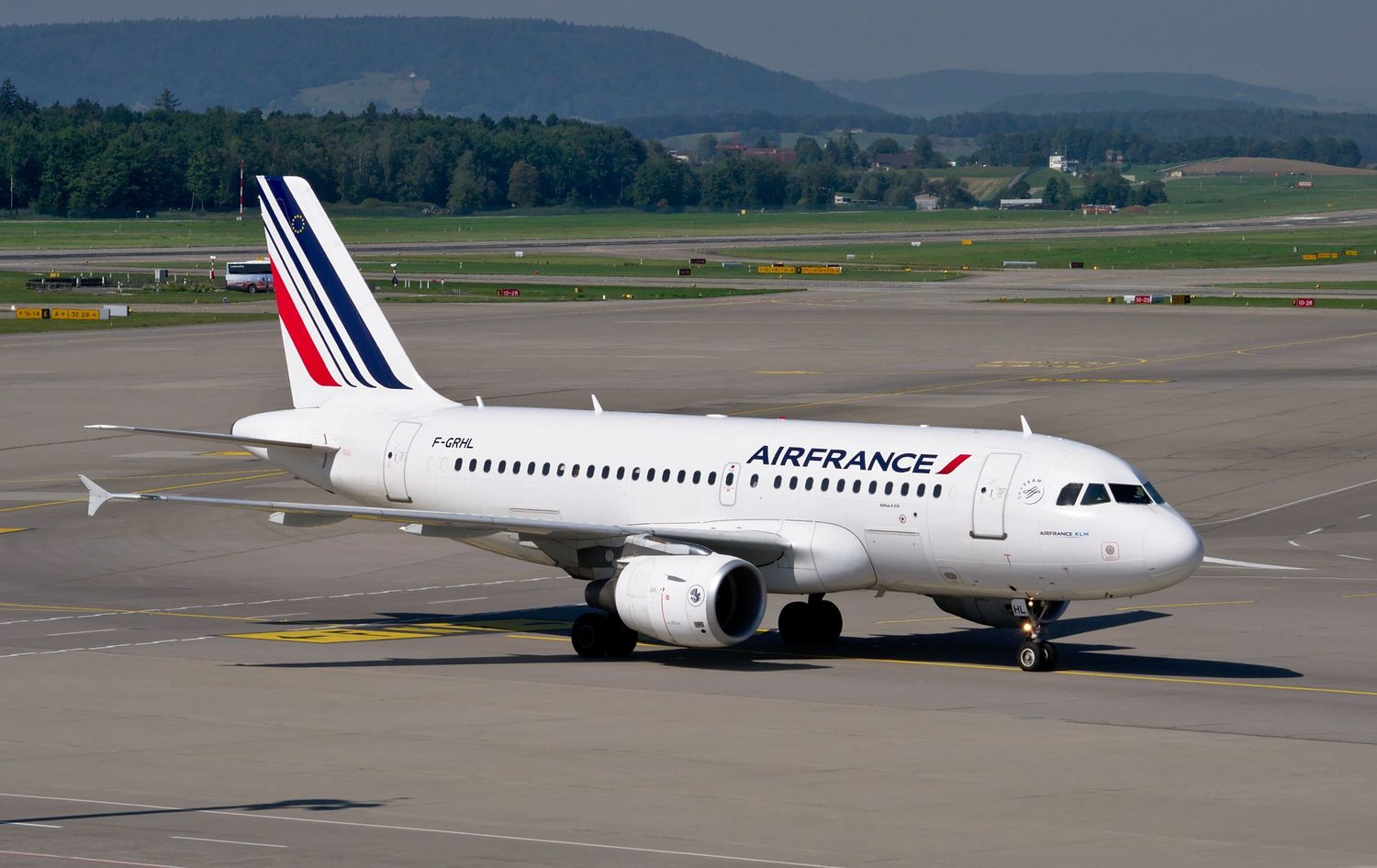 An Air France Airbus A318 passenger aircraft on the tarmac at an airport with mountains visible in the background.