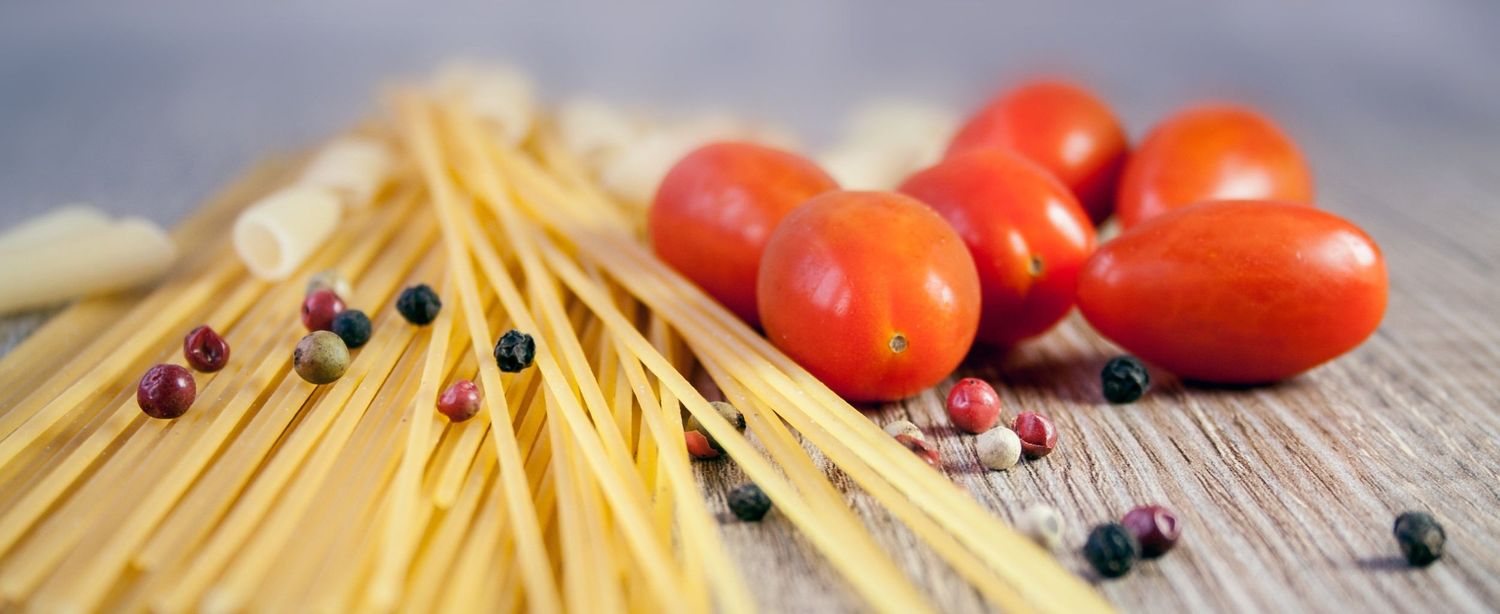 Fresh ingredients including tomatoes, pasta, and berries arranged on rustic wooden surfaces in a culinary composition.