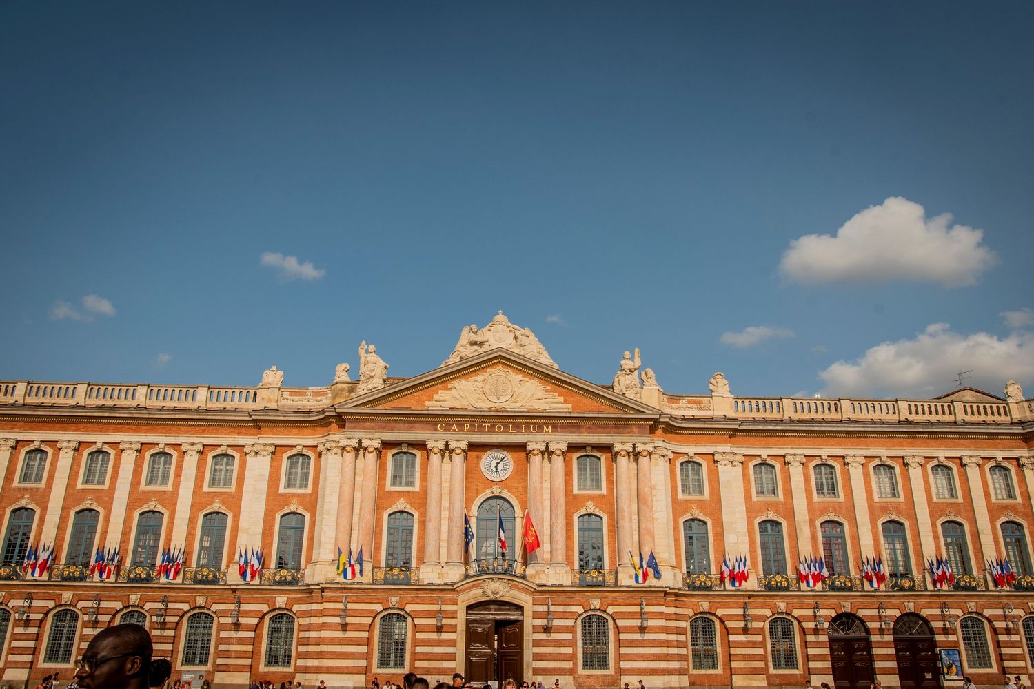 Historic Capitol Building in Toulouse features ornate peach-colored facade with classical architecture under blue sky.
