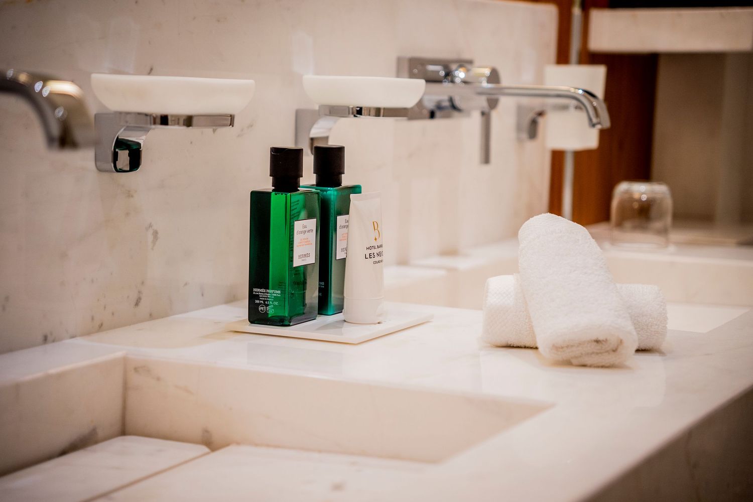 Green toiletry bottles and white towels arranged on a clean marble bathroom counter with modern chrome fixtures.