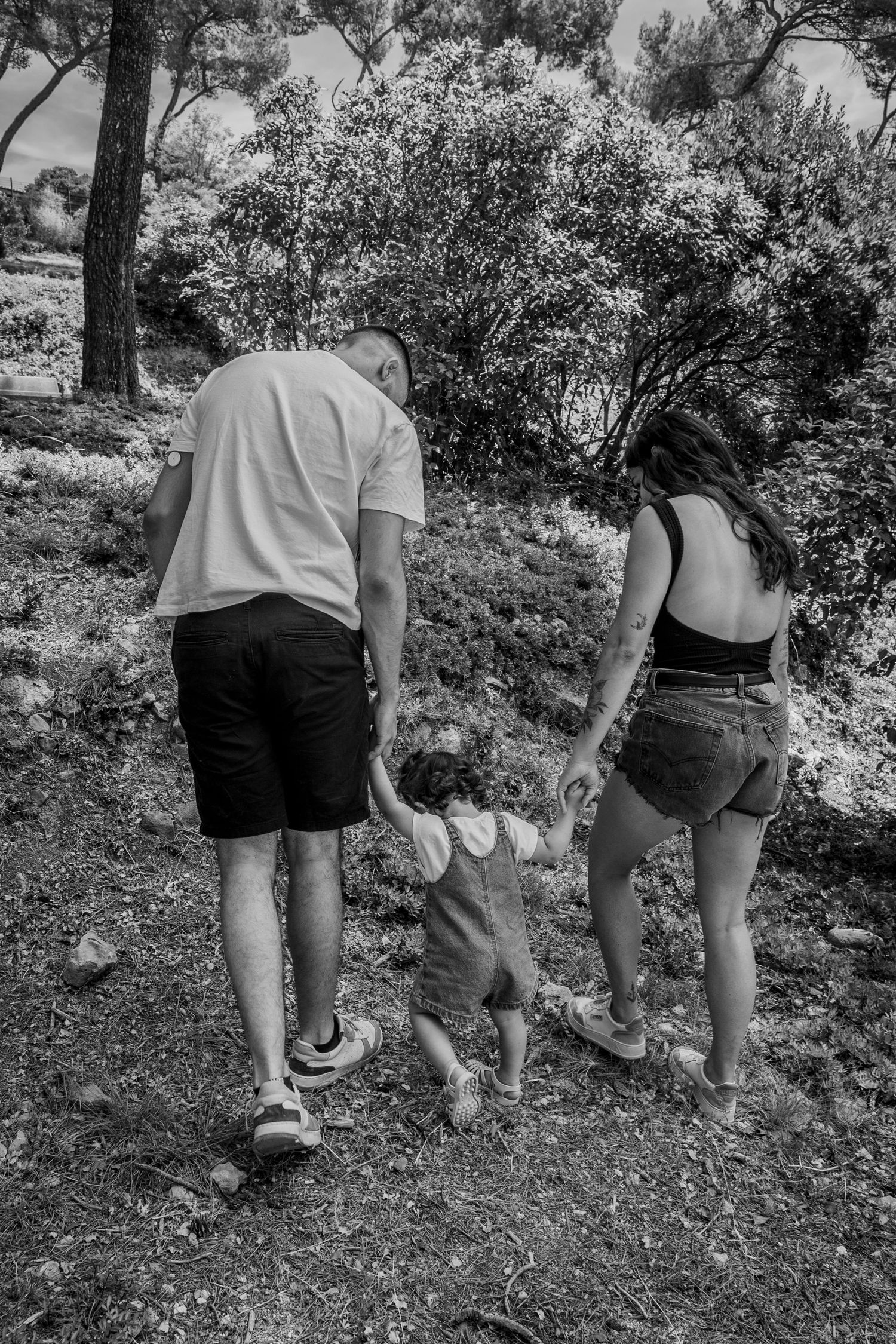 Family walking together on nature trail holding toddler's hands in black and white photograph.