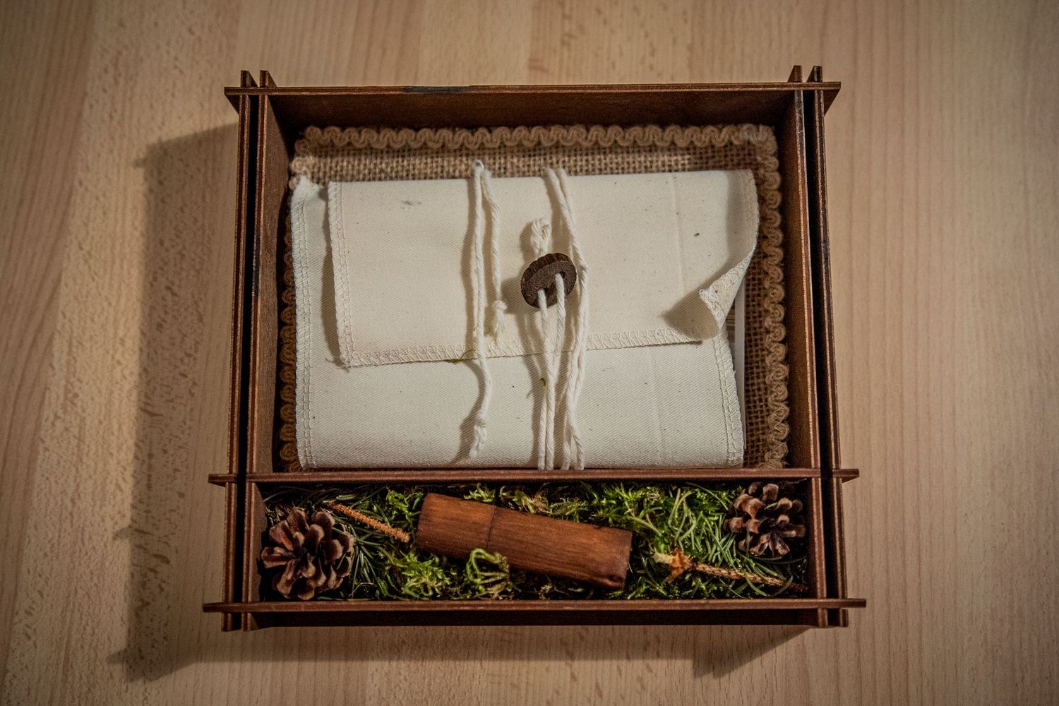 Vintage wooden box with two compartments displaying white fabric and spices with cinnamon stick below.
