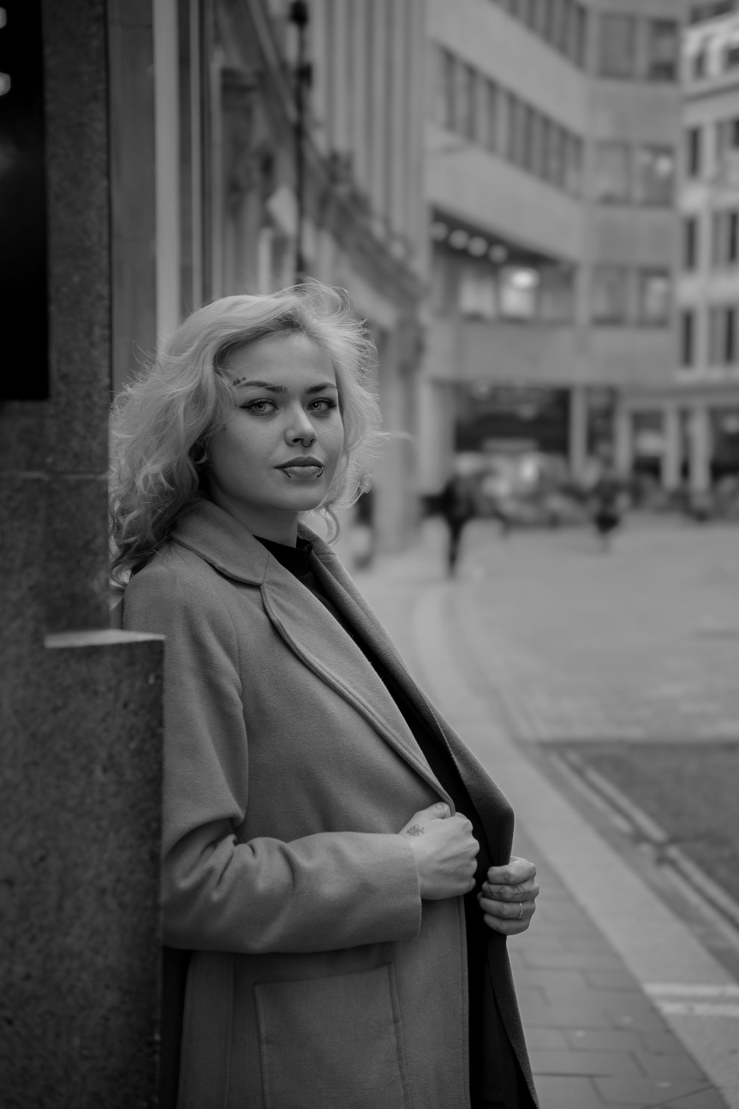 Person in beige coat poses on urban street in black and white photography series.
