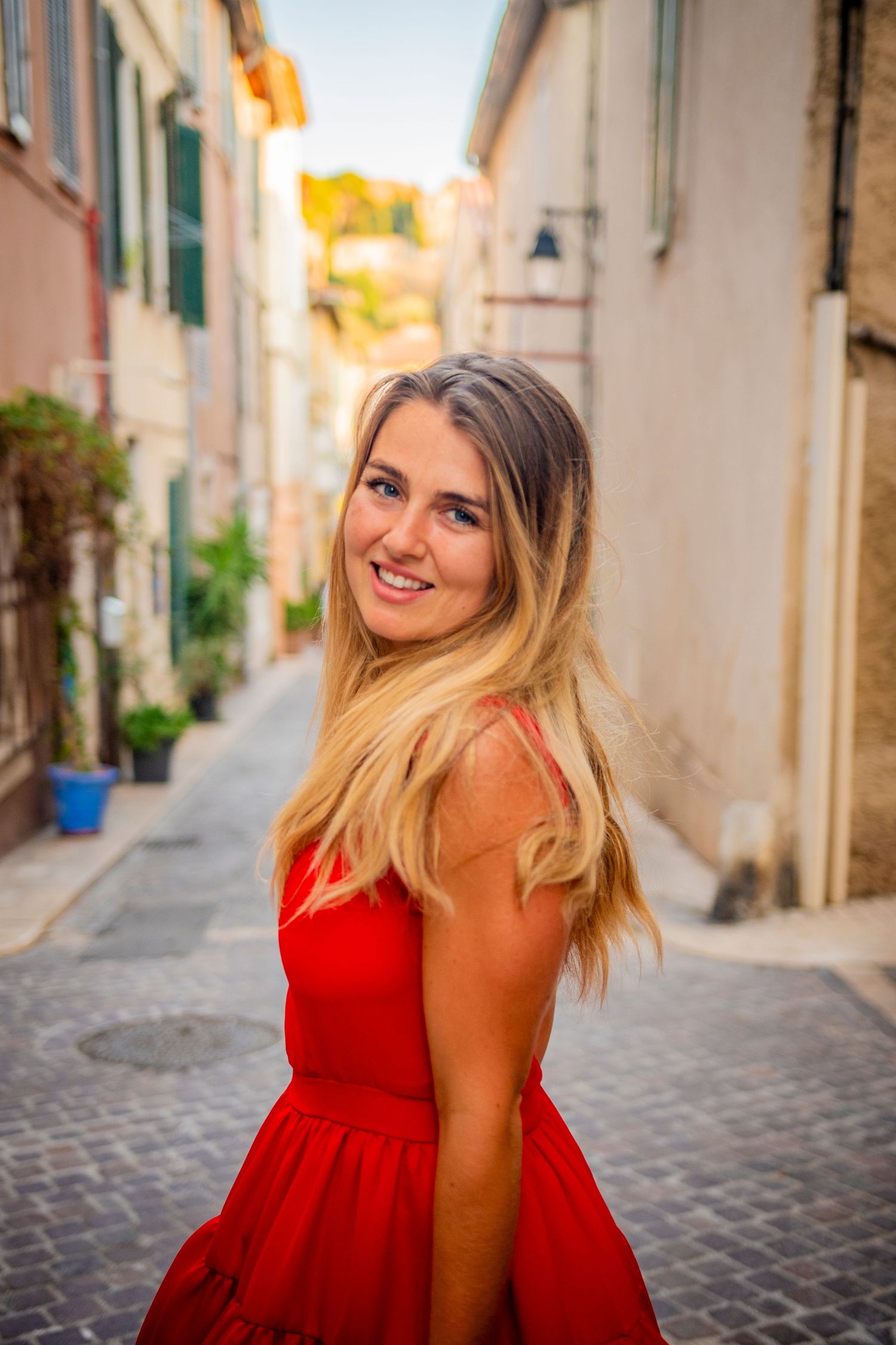 Woman in red dress smiling on charming European cobblestone street.