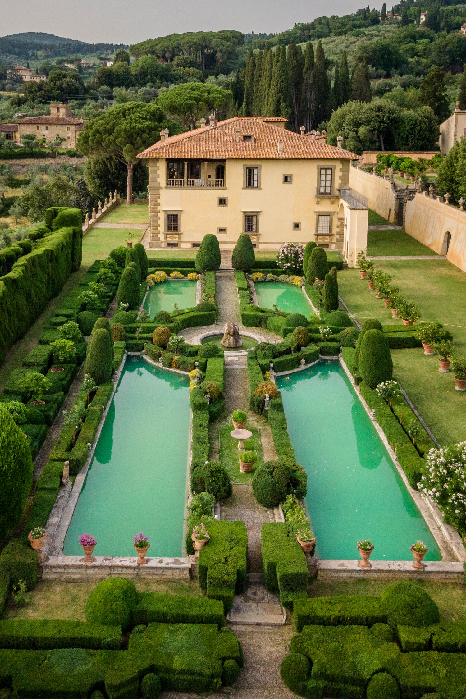 Aerial view of an Italian Renaissance villa with formal gardens featuring symmetrical hedges and turquoise reflecting pools in Tuscany.