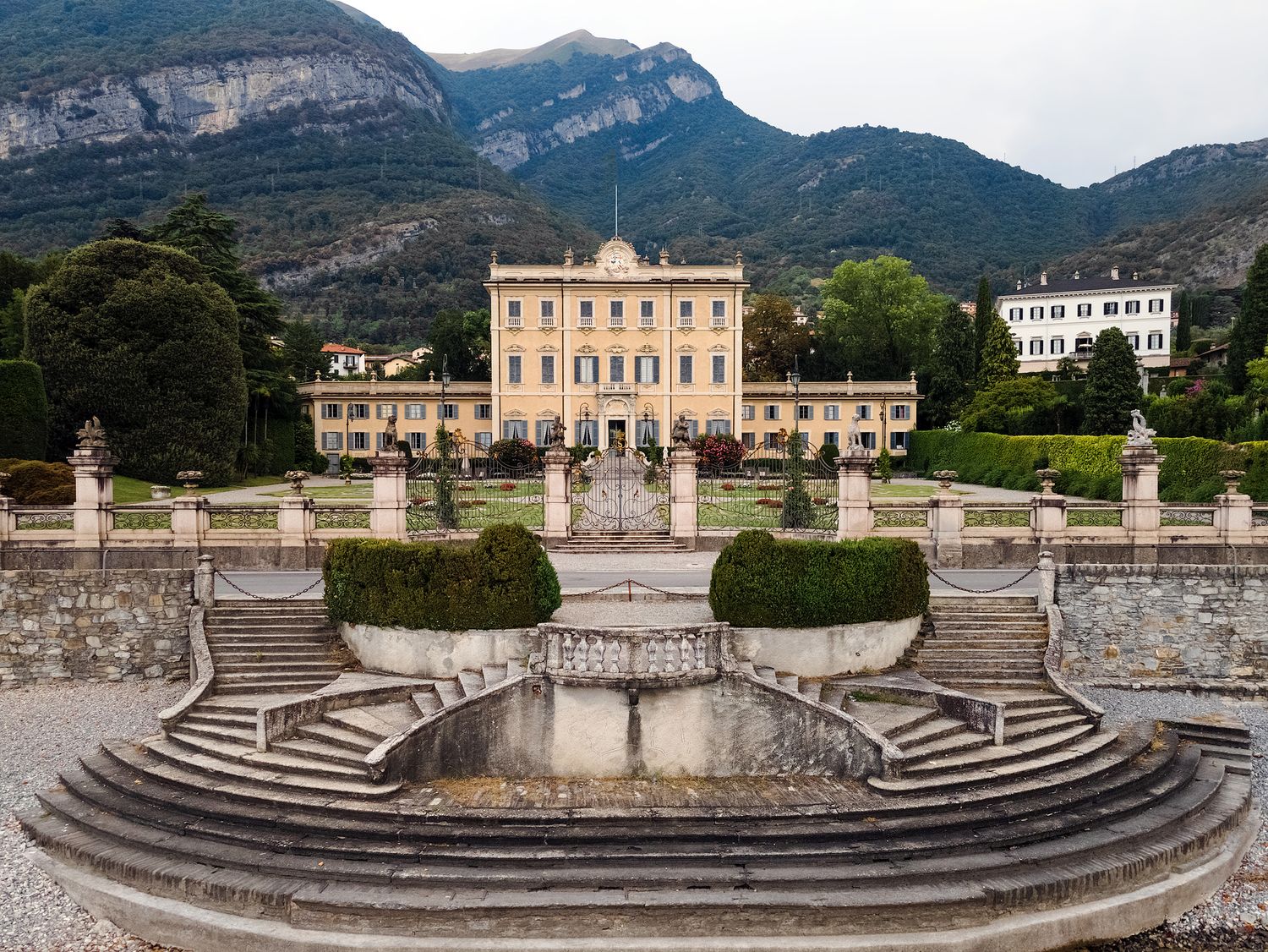 Elegant Italian villa with formal gardens, fountain, and mountain backdrop on Lake Como.