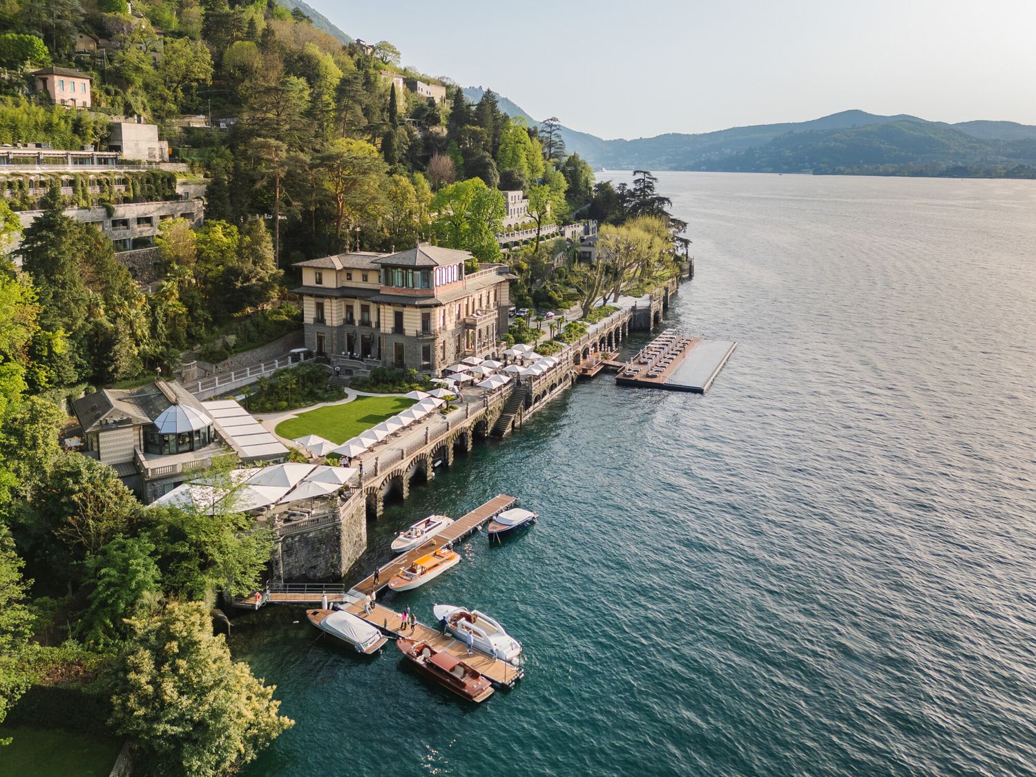 Aerial view of a luxurious lakeside villa with private dock, boats, and lush greenery on Lake Maggiore, Italy.