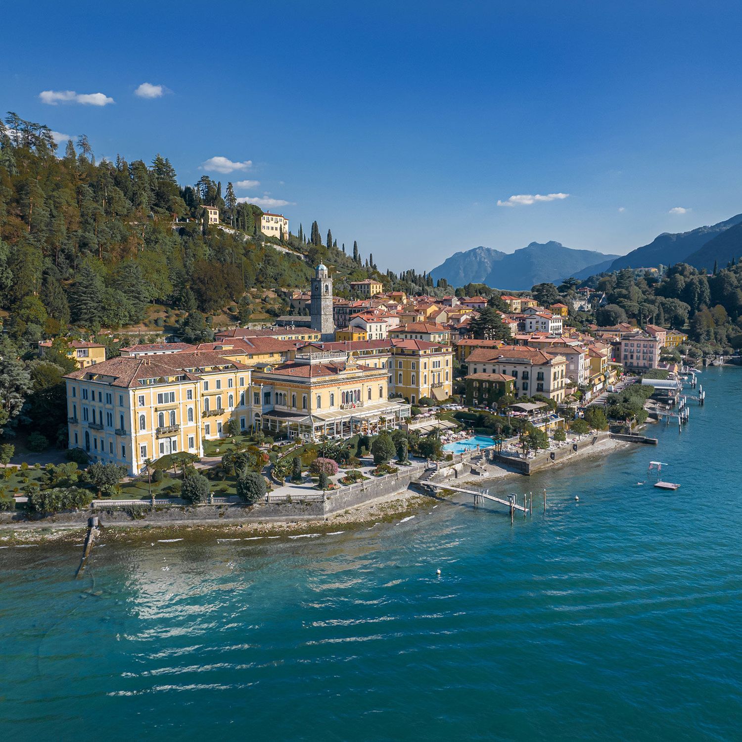 Aerial view of a picturesque Italian lakeside village with colorful buildings, a bell tower, and turquoise waters.