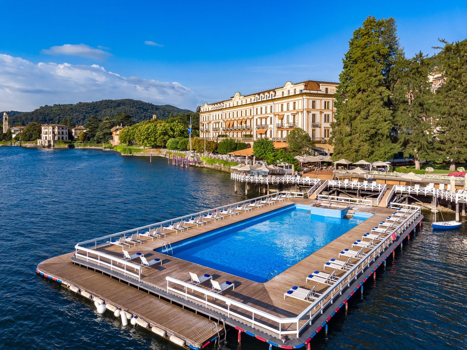 Luxury hotel on Lake Como with floating pool, white lounge chairs, and elegant yellow facade surrounded by lush greenery.
