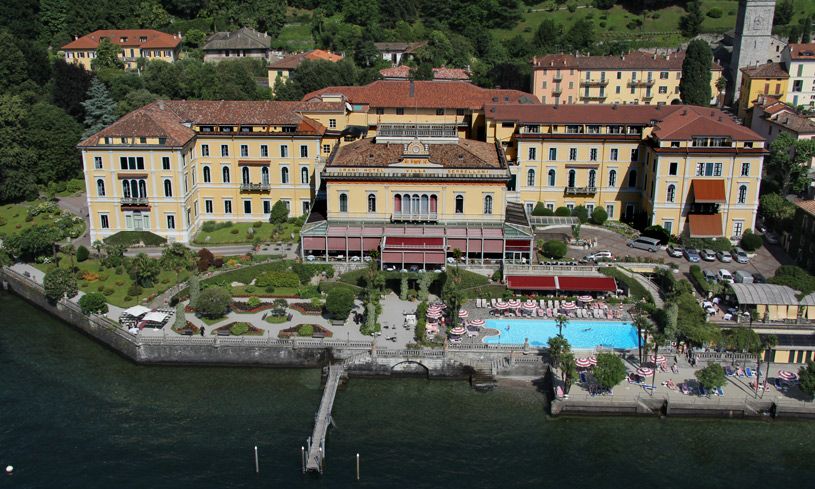 Aerial view of a luxury lakeside hotel with yellow facade, pool, and dock on Lake Como, Italy.