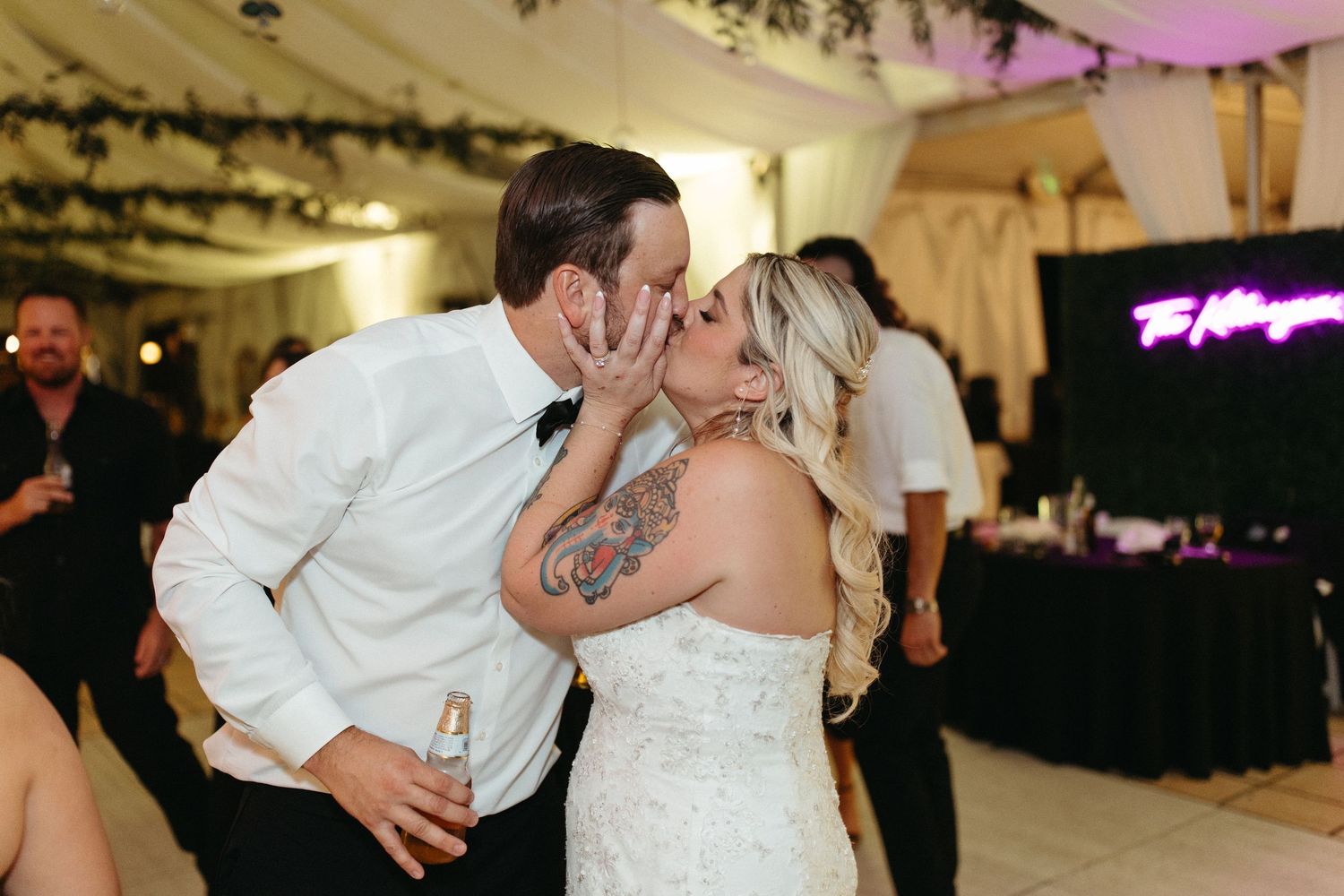 Tattooed bride and groom share a passionate kiss on the dance floor during their wedding reception.