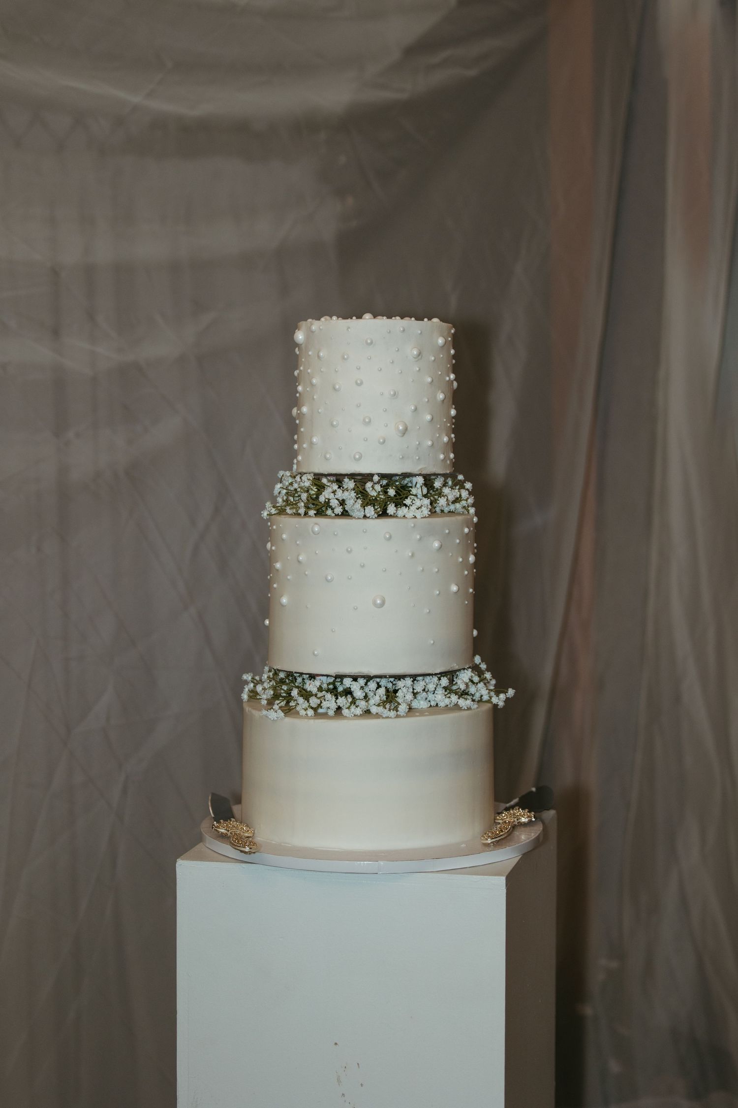 An elegant four-tier white wedding cake adorned with pearl dots and delicate baby's breath flowers.