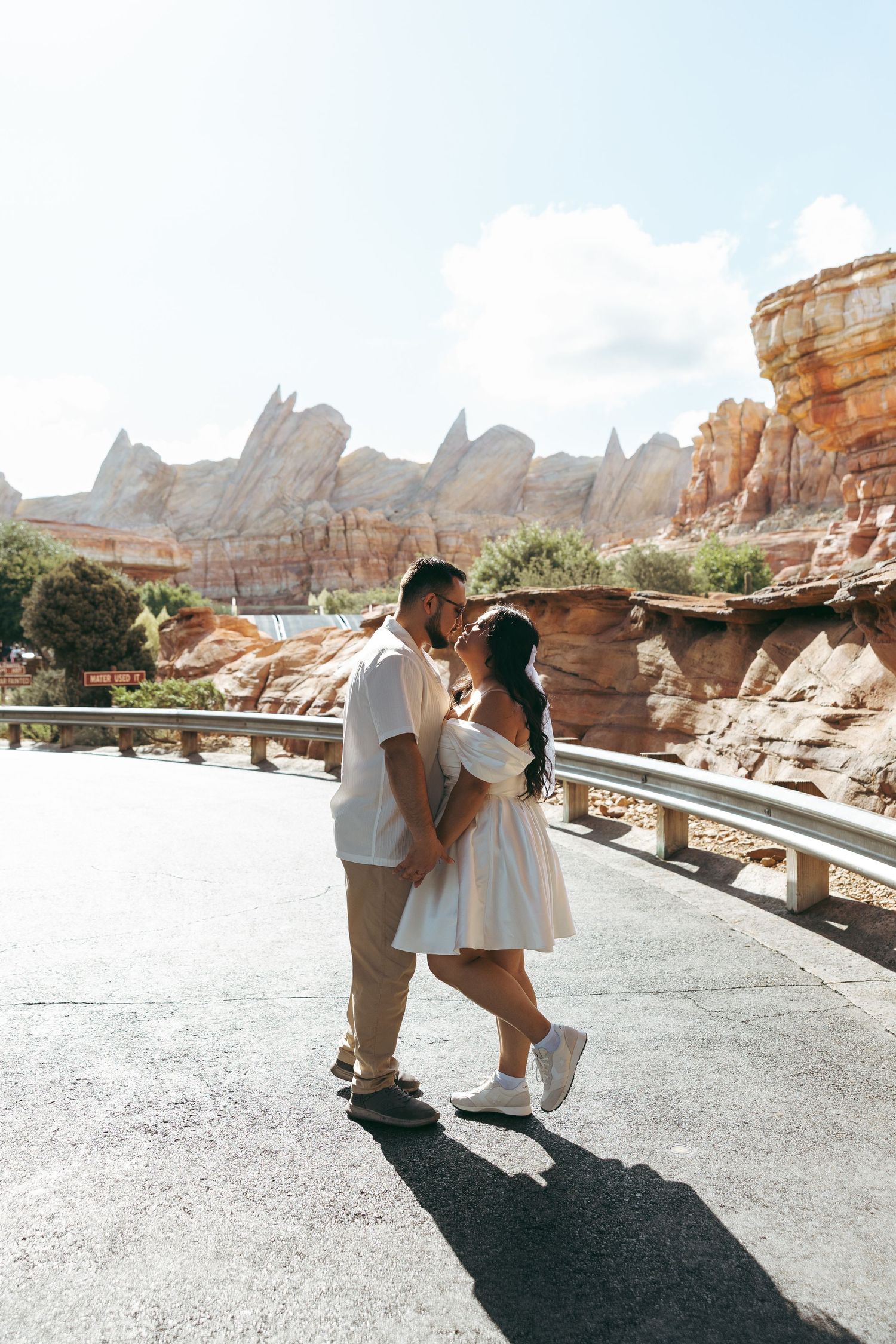 Couple sharing a kiss on a scenic road with red rock formations backdrop.
