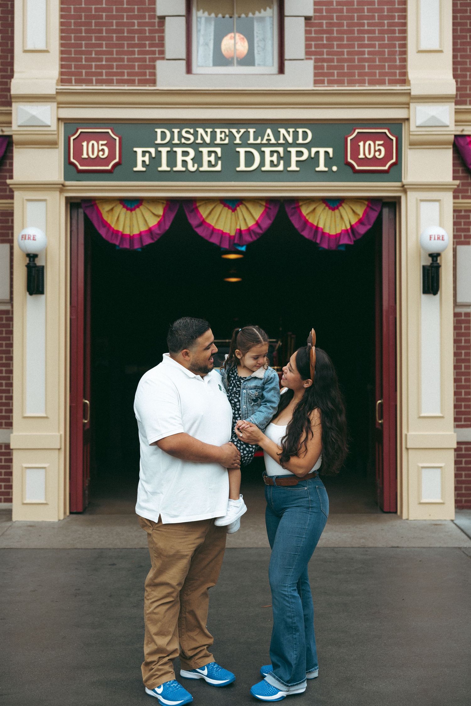 Family of three posing in front of Disneyland Fire Dept. No. 105 on Main Street, U.S.A. at Disneyland.
