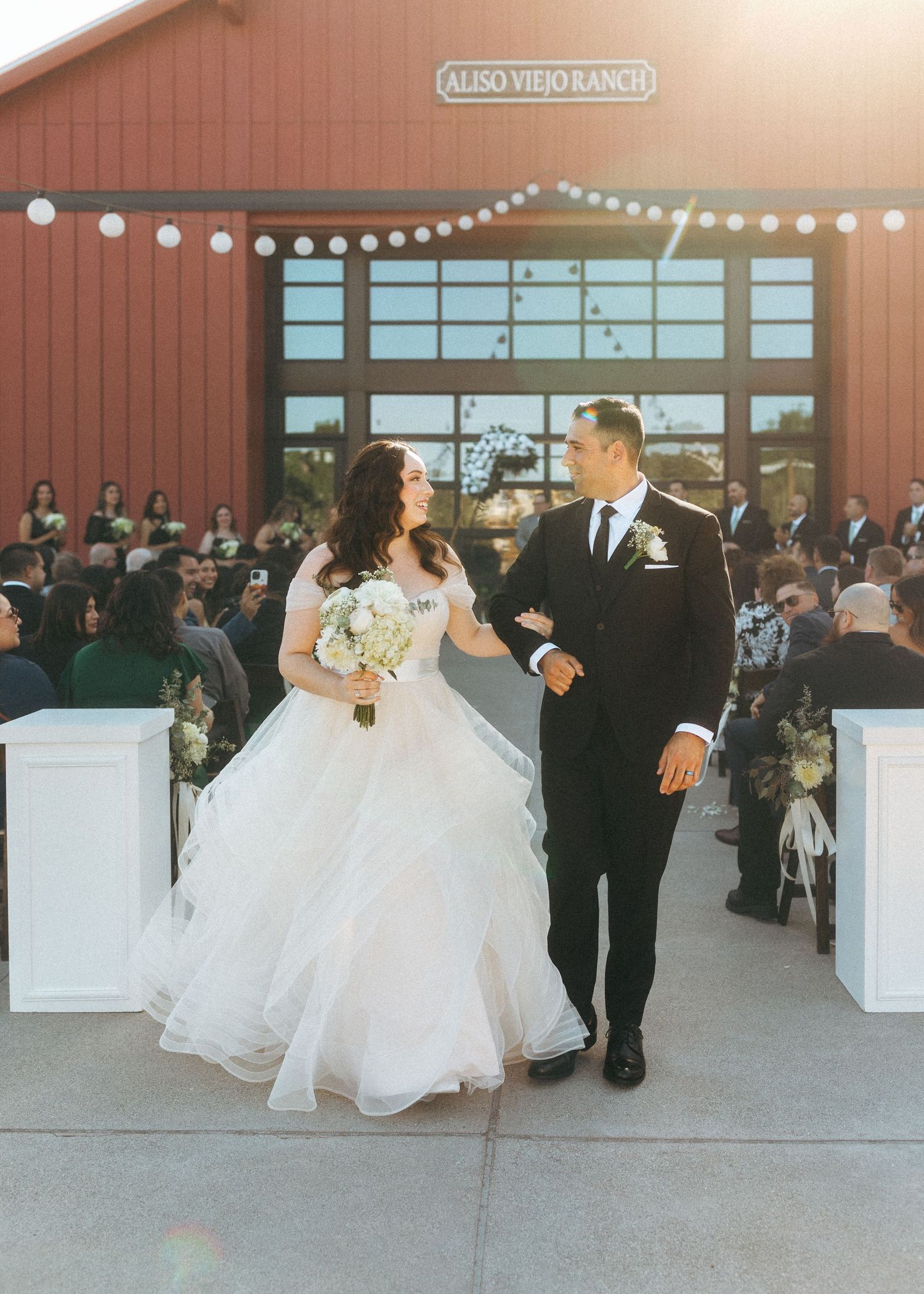 A bride and groom walk triumphantly down the aisle at Aliso Viejo Ranch wedding venue with guests cheering.