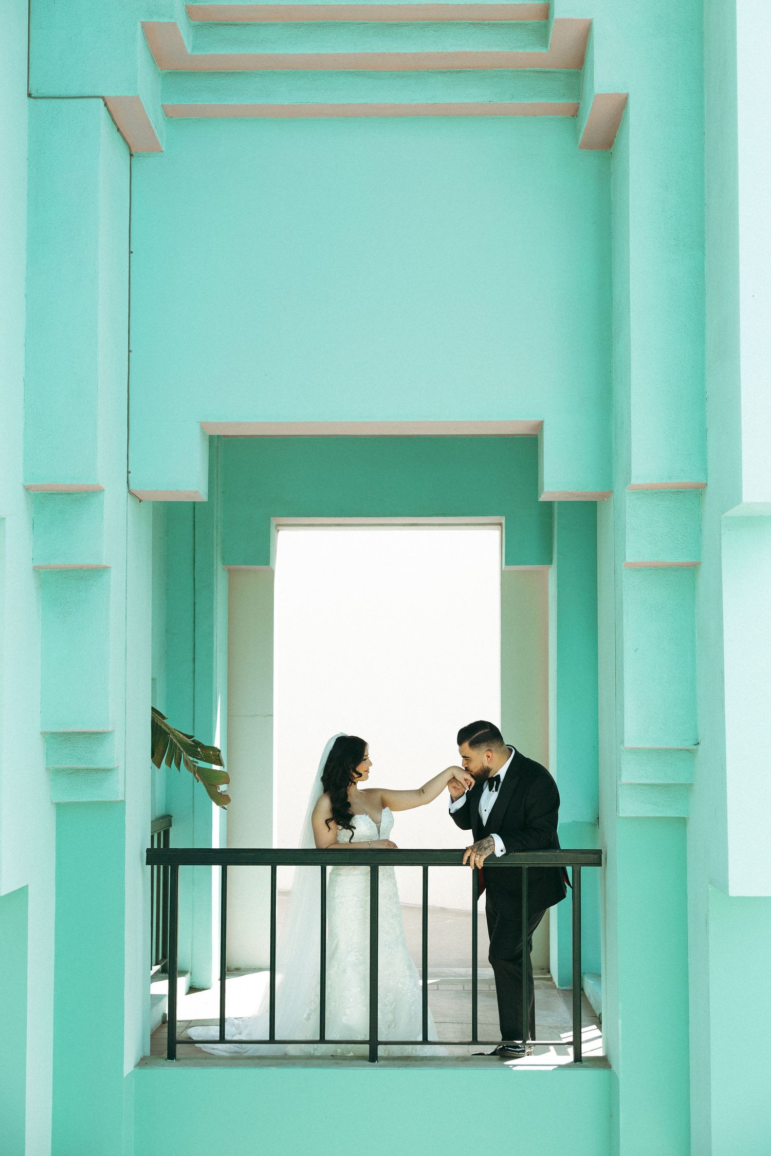Elegant couple in wedding attire on a mint green architectural balcony.