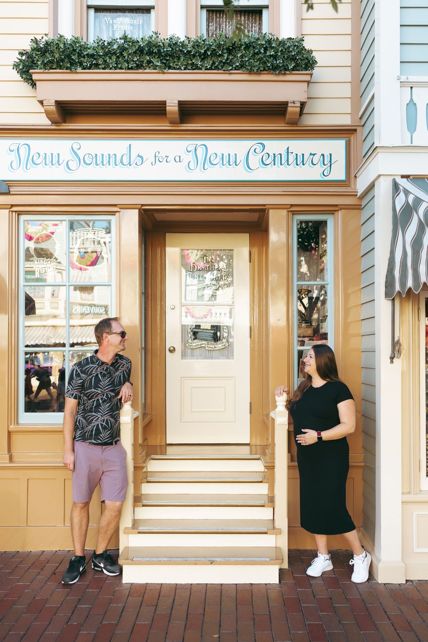 Couple posing outside a charming shop with 'New Sounds for a New Century' sign at a theme park.